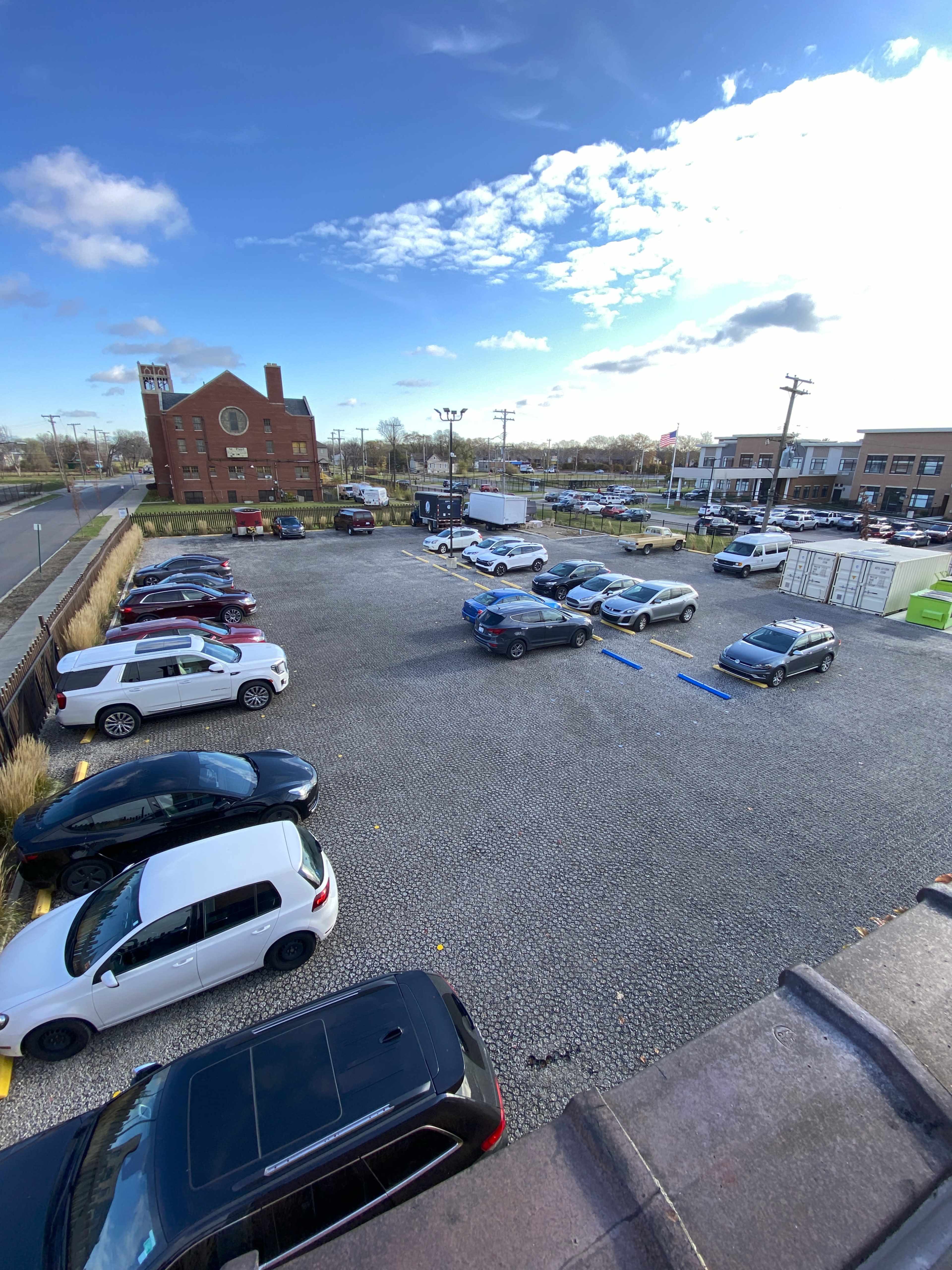 A parking lot with several parked cars, a visible building in the background, and a clear blue sky.