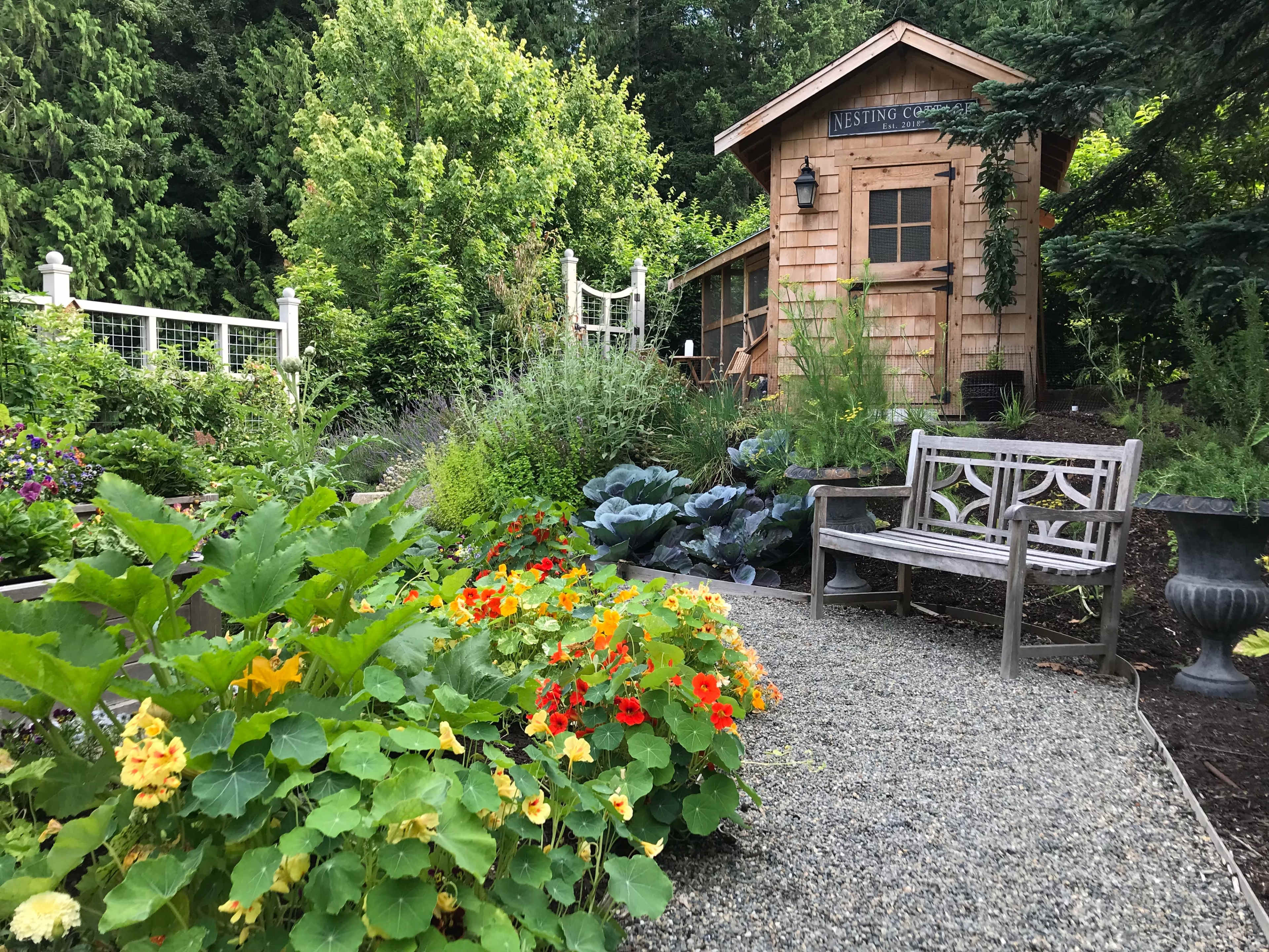 A wooden storage shed surrounded by lush greenery and a flower bed with vibrant orange and yellow flowers.