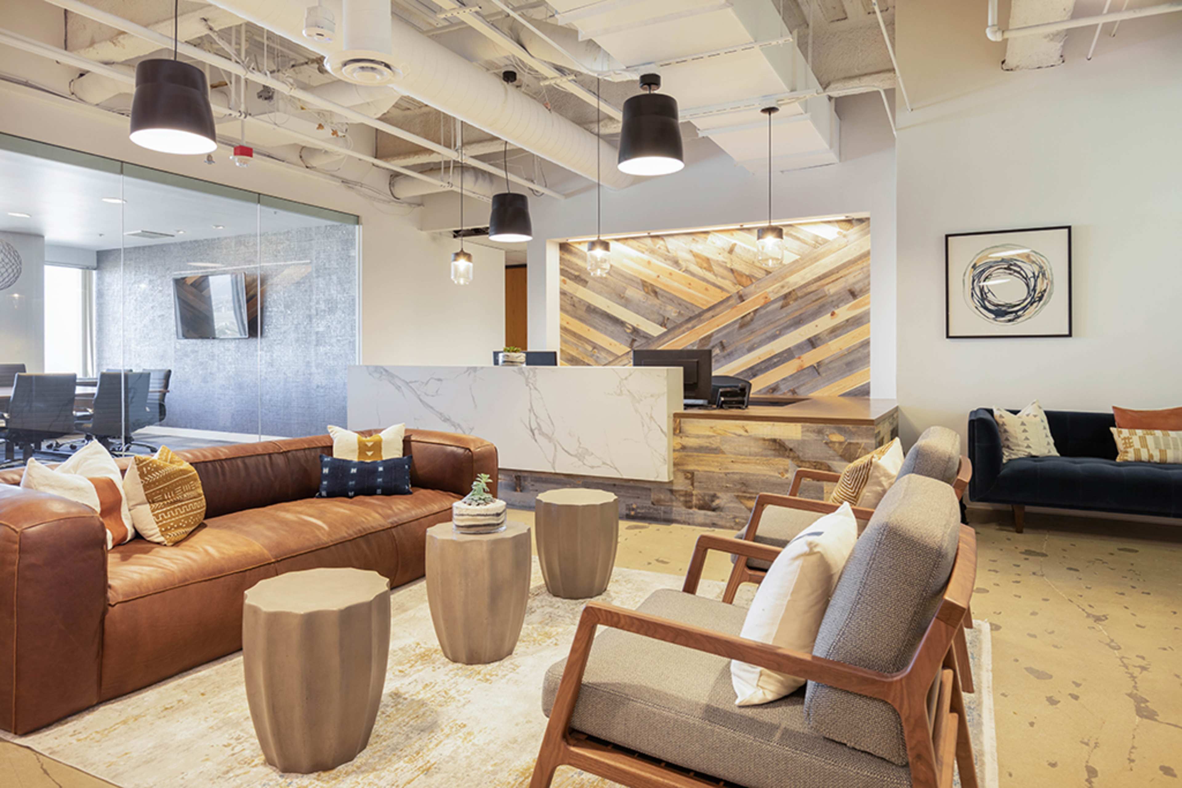 A modern office reception area featuring a brown leather sofa, wooden coffee tables, and a marble reception desk with a rustic wooden backdrop.
