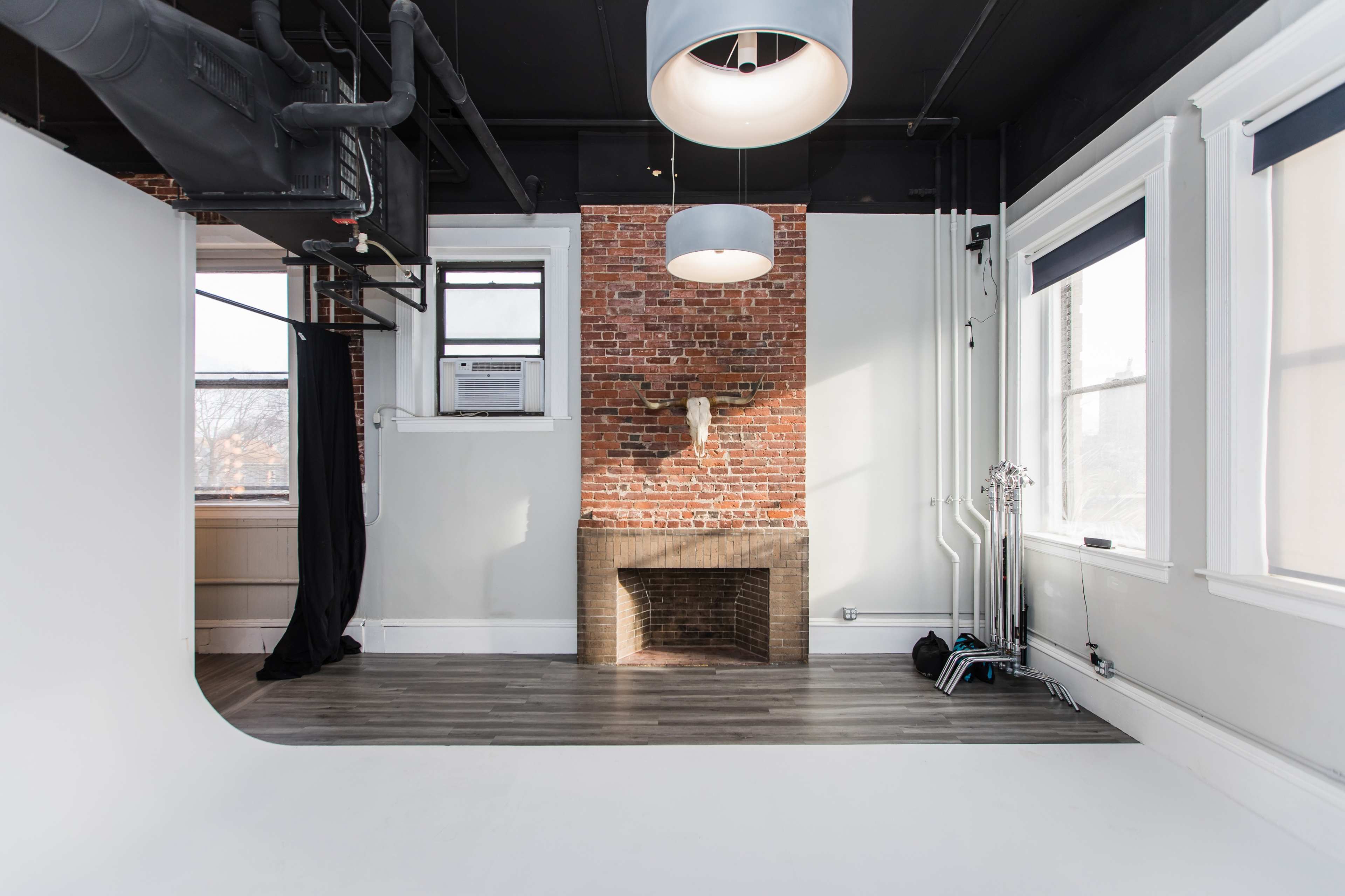 A spacious room with a brick wall, a fireplace, two light fixtures hanging from the ceiling, and a backdrop setup.