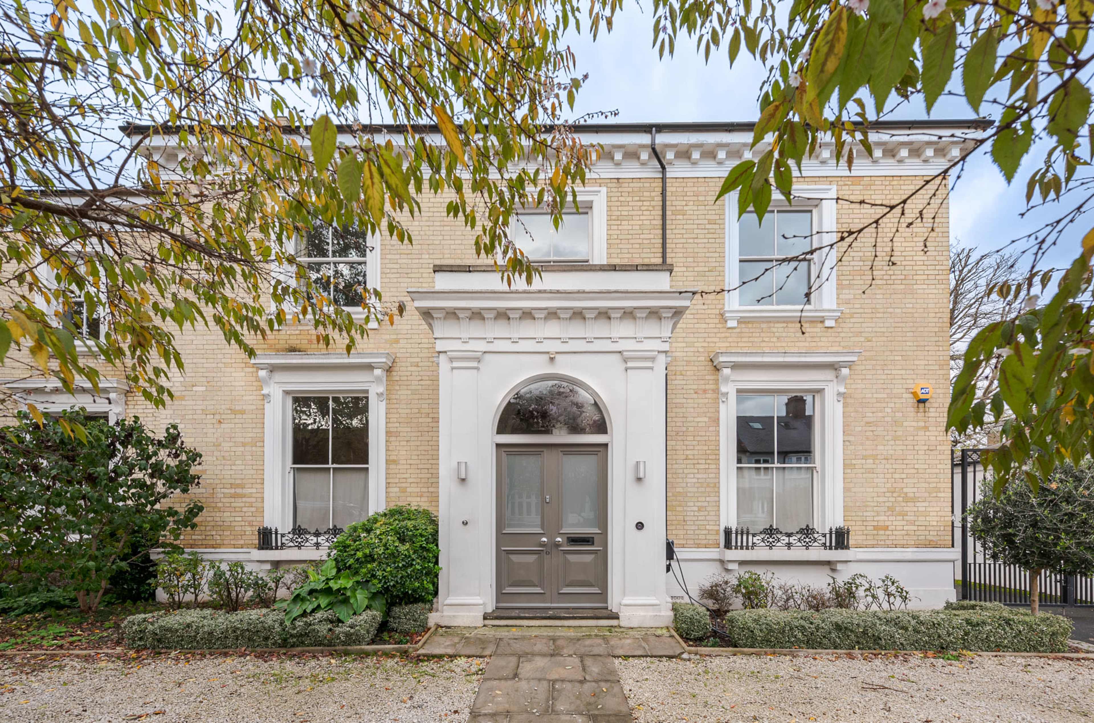 A two-story brick house with a symmetrical facade, featuring large windows, a central arched doorway, and a neatly landscaped front garden.