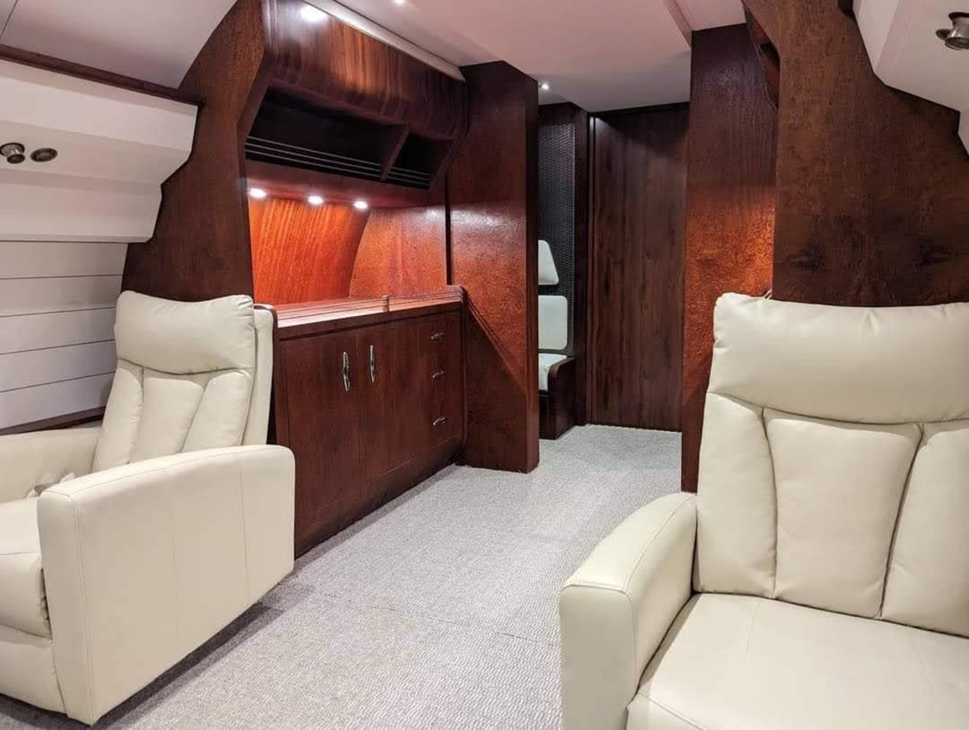 A modern interior space featuring two cream-colored armchairs, wooden paneling, and well-lit cabinetry.