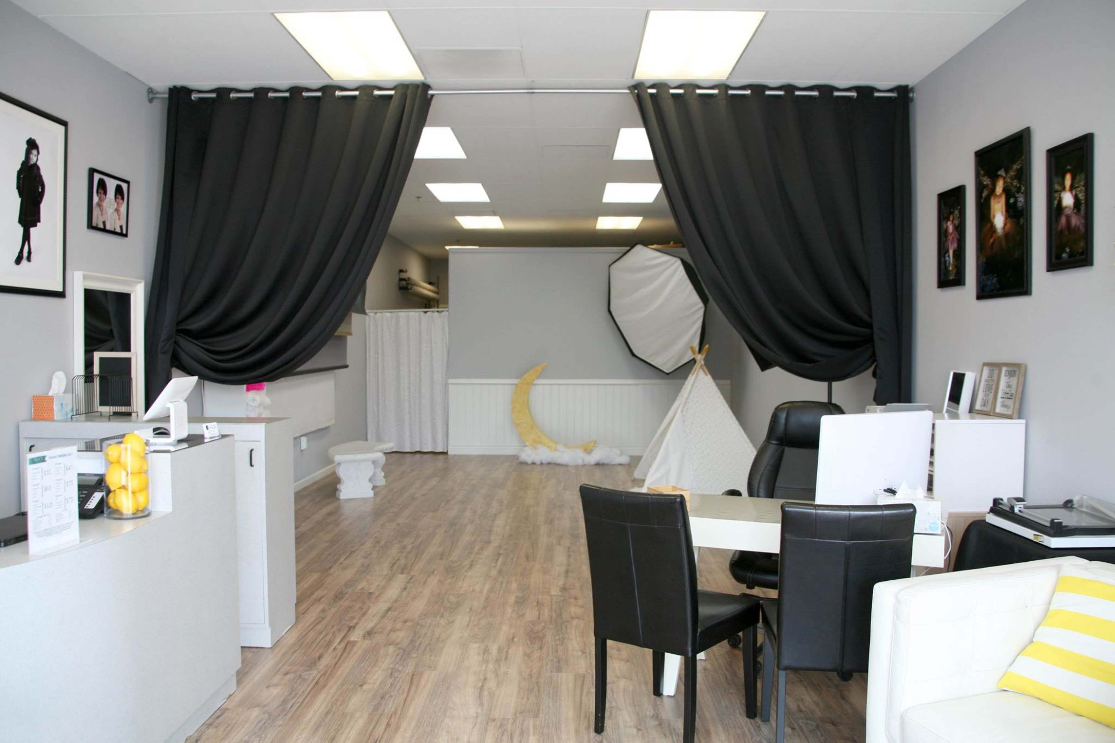 A spacious photography studio with grey walls, black curtains, and various photography props arranged throughout.