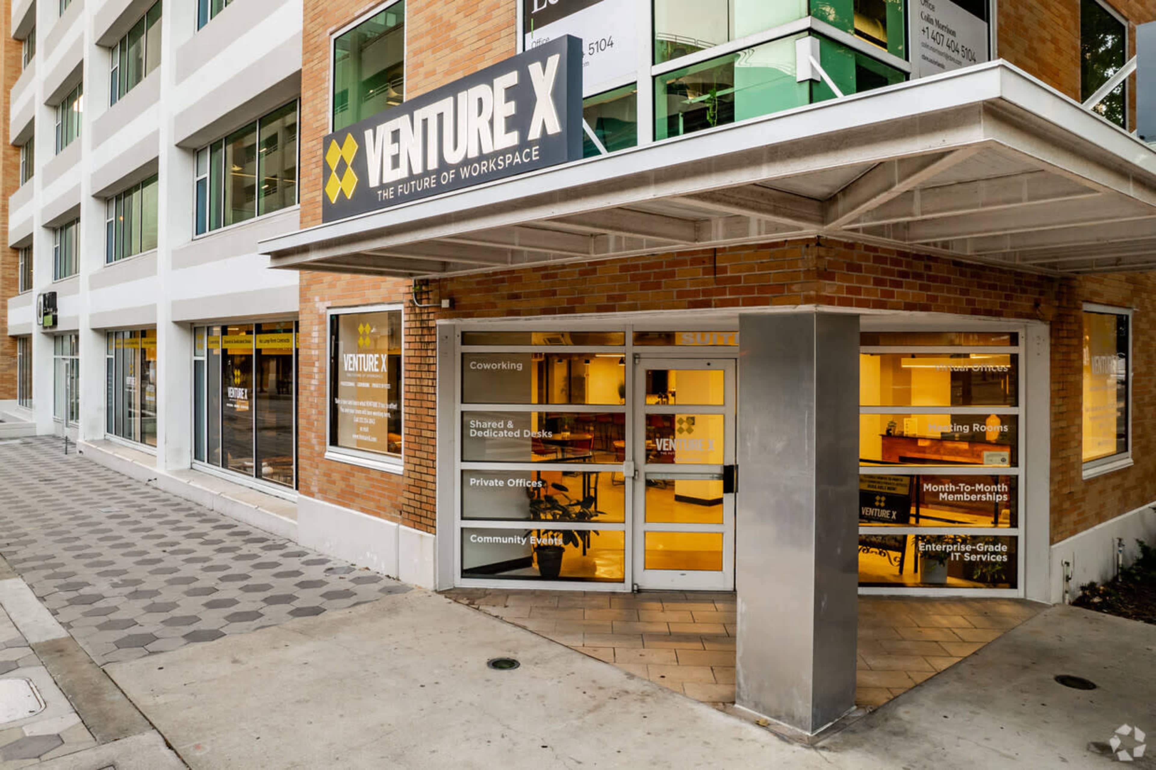 The entrance to Venture X, a modern coworking space, featuring large glass doors and a sign overhead.