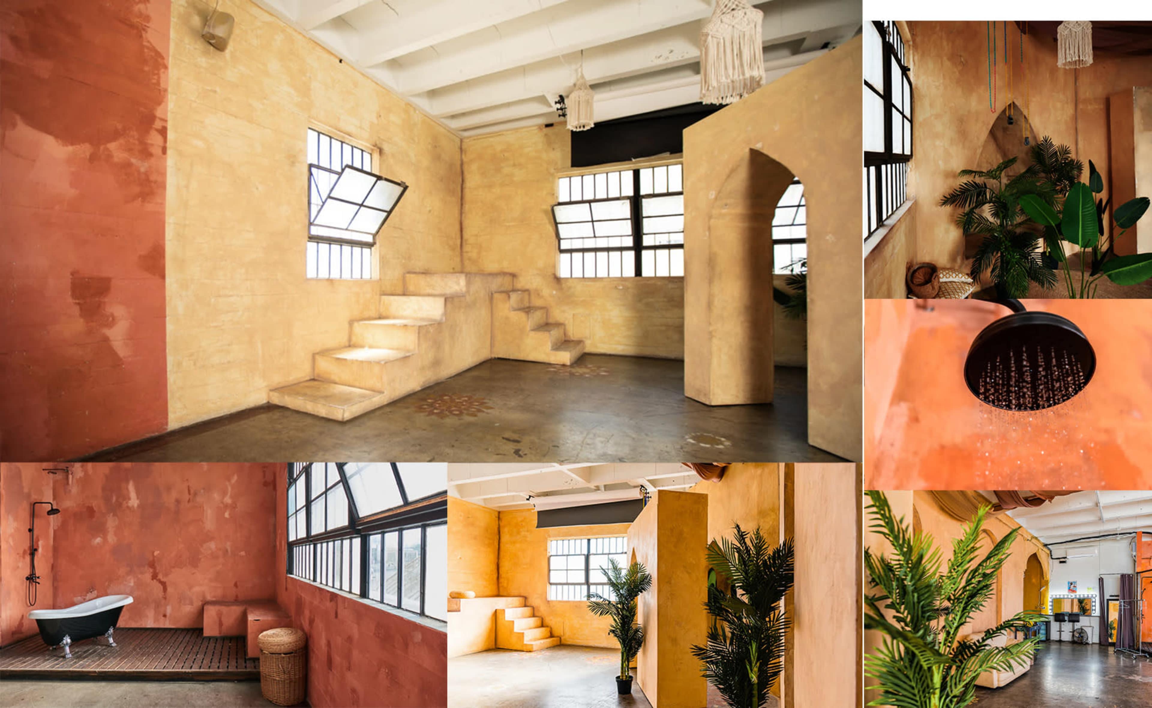 A spacious room with textured orange and yellow walls, large windows, a staircase, and various plants decorating the corners.