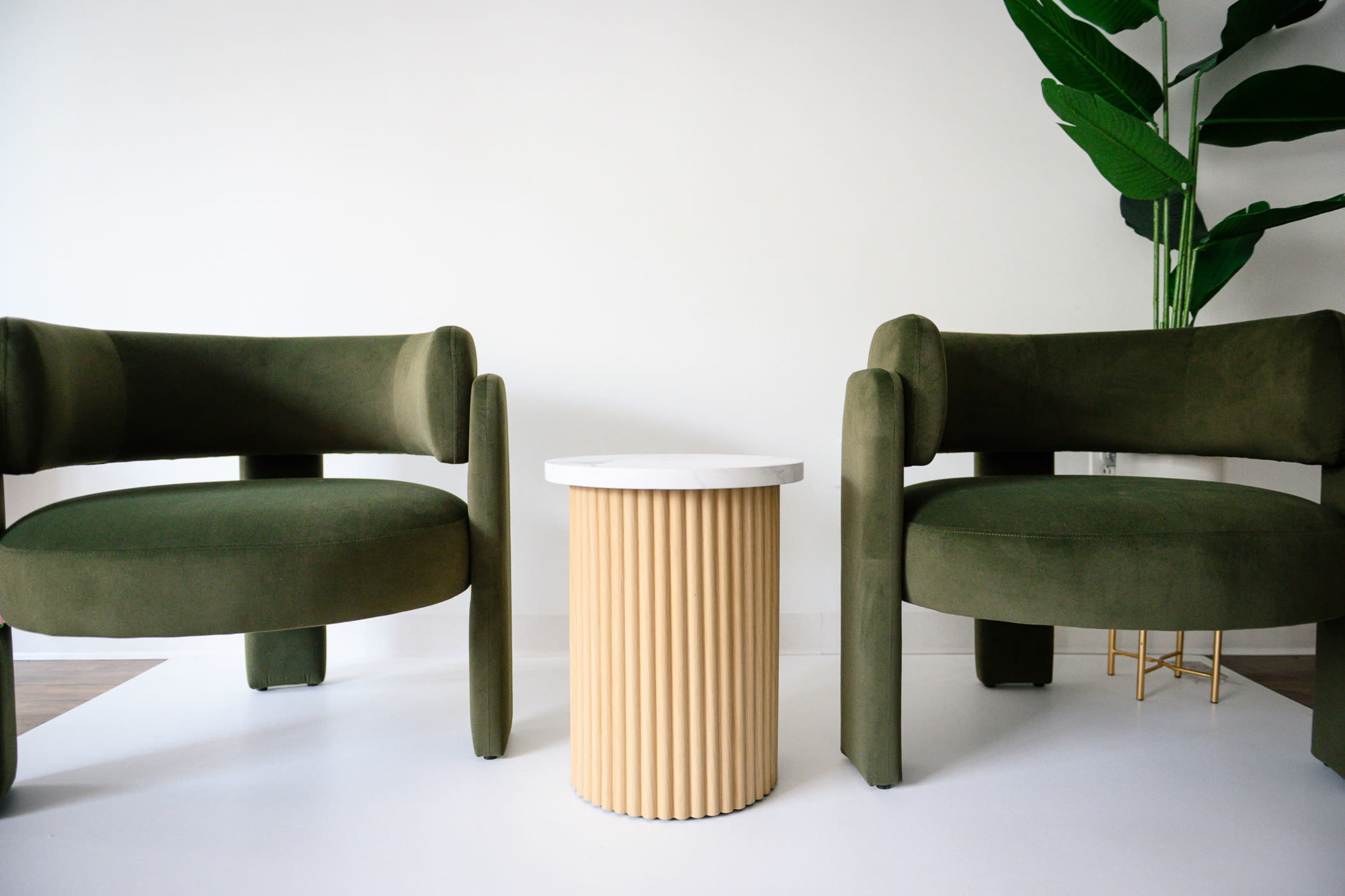 The image features two olive-green chairs facing each other with a striped beige and white side table positioned between them.