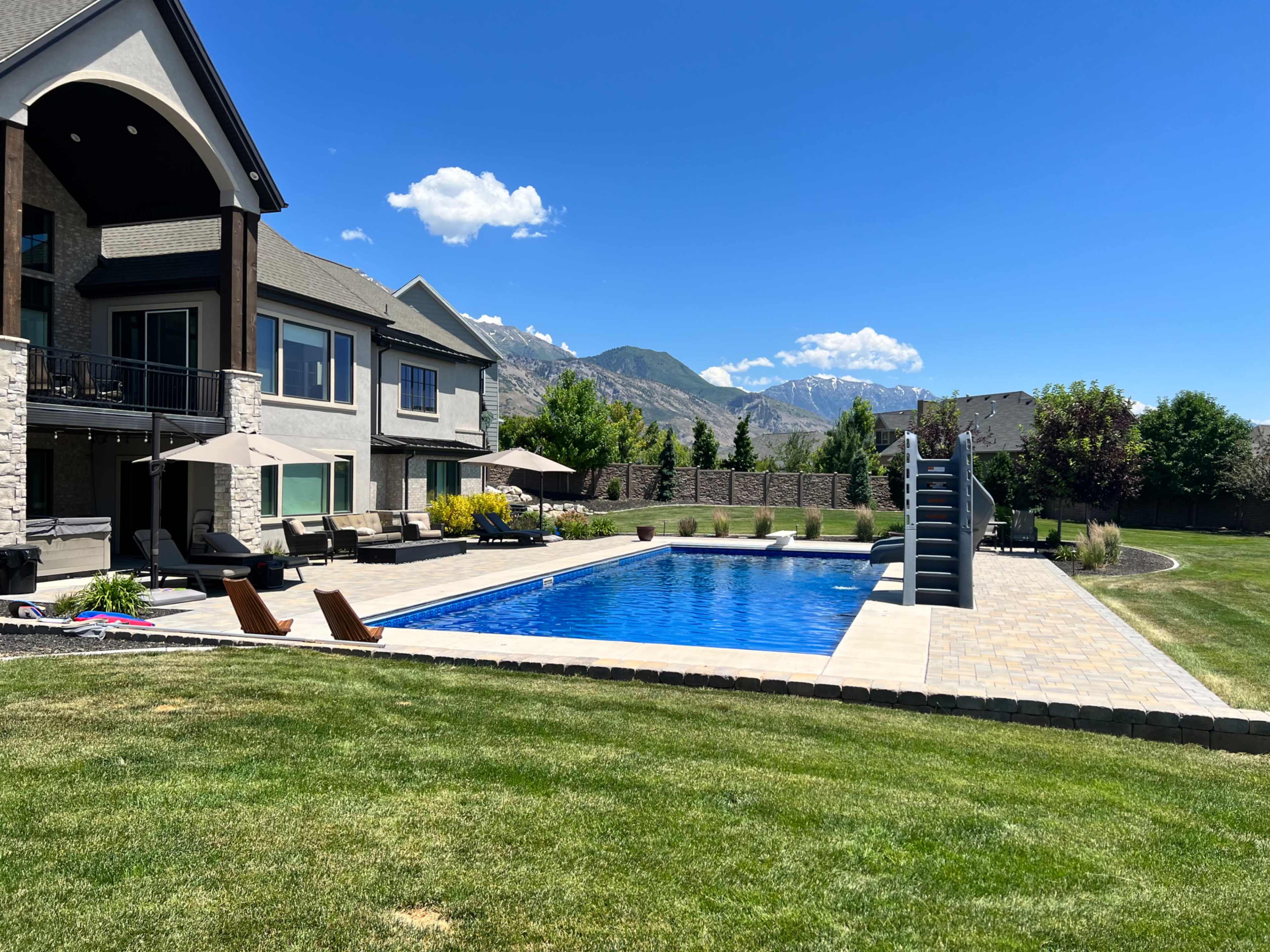 A spacious backyard features a rectangular swimming pool, lounge chairs, and a multi-level home overlooking a mountain landscape.