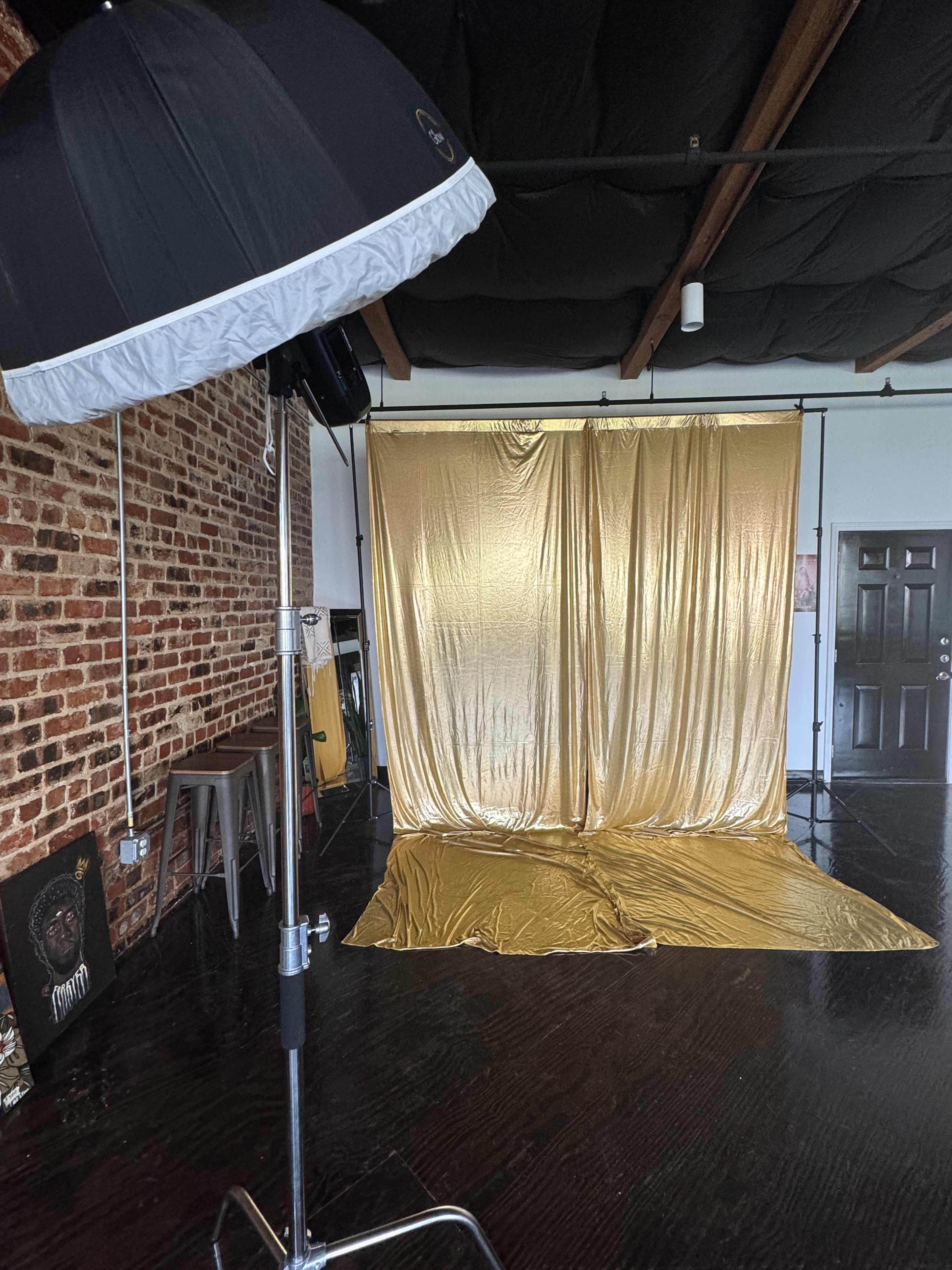 The image shows a photography studio with a gold backdrop and a softbox light set up in front of it.