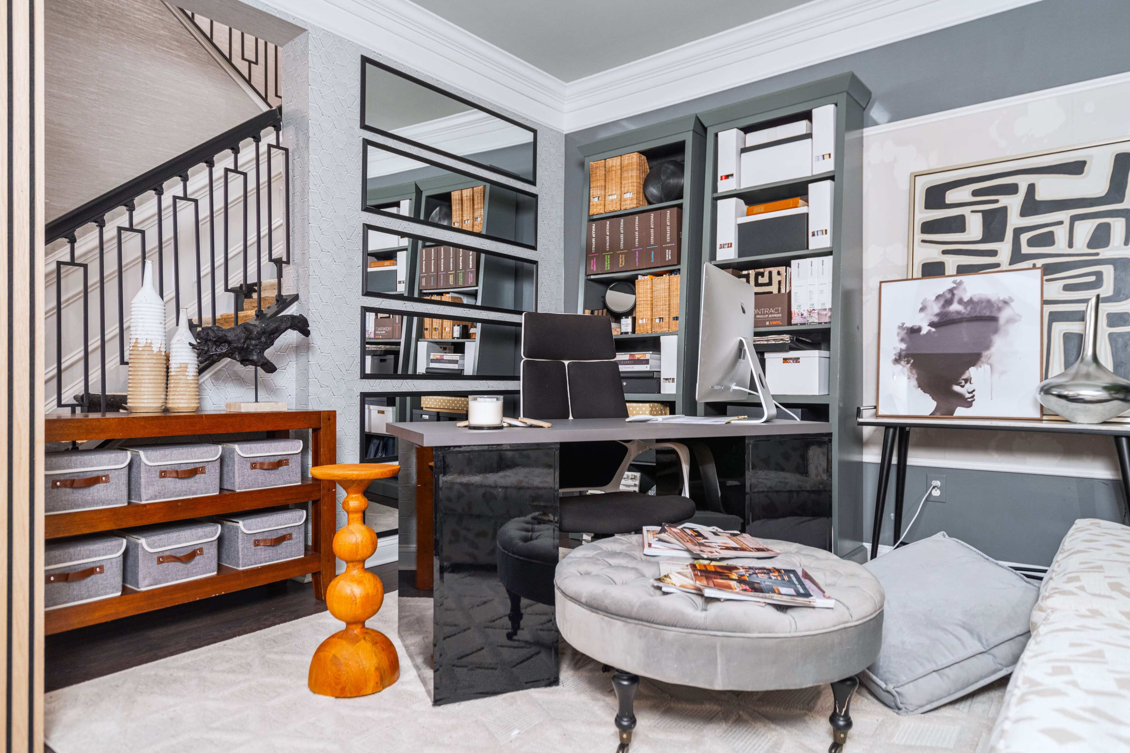 A stylish home office featuring a sleek black desk, organized storage boxes, a modern chair, and a staircase in a well-decorated space.