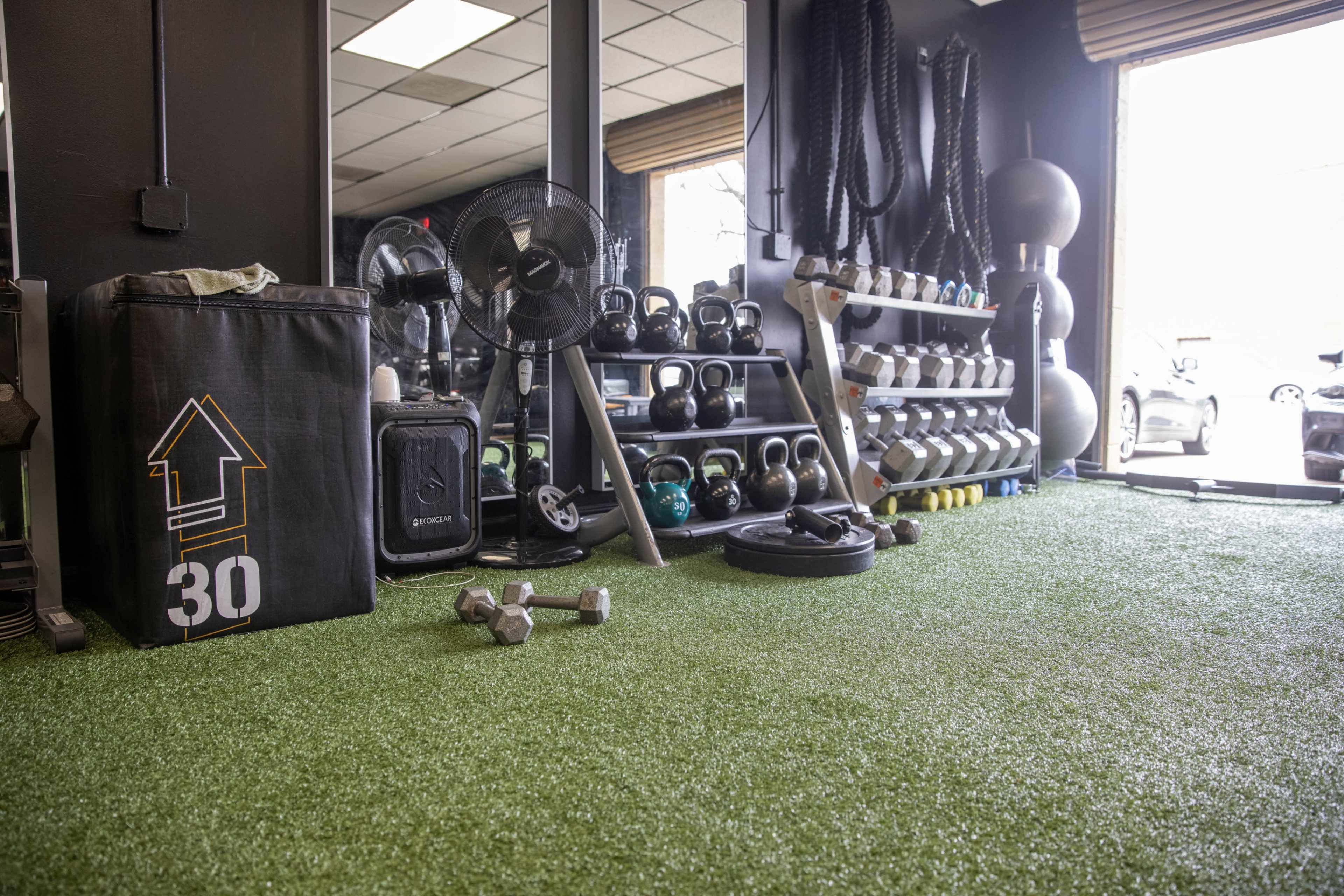 A gym area featuring a variety of weights, kettlebells, and fitness equipment on green turf flooring.