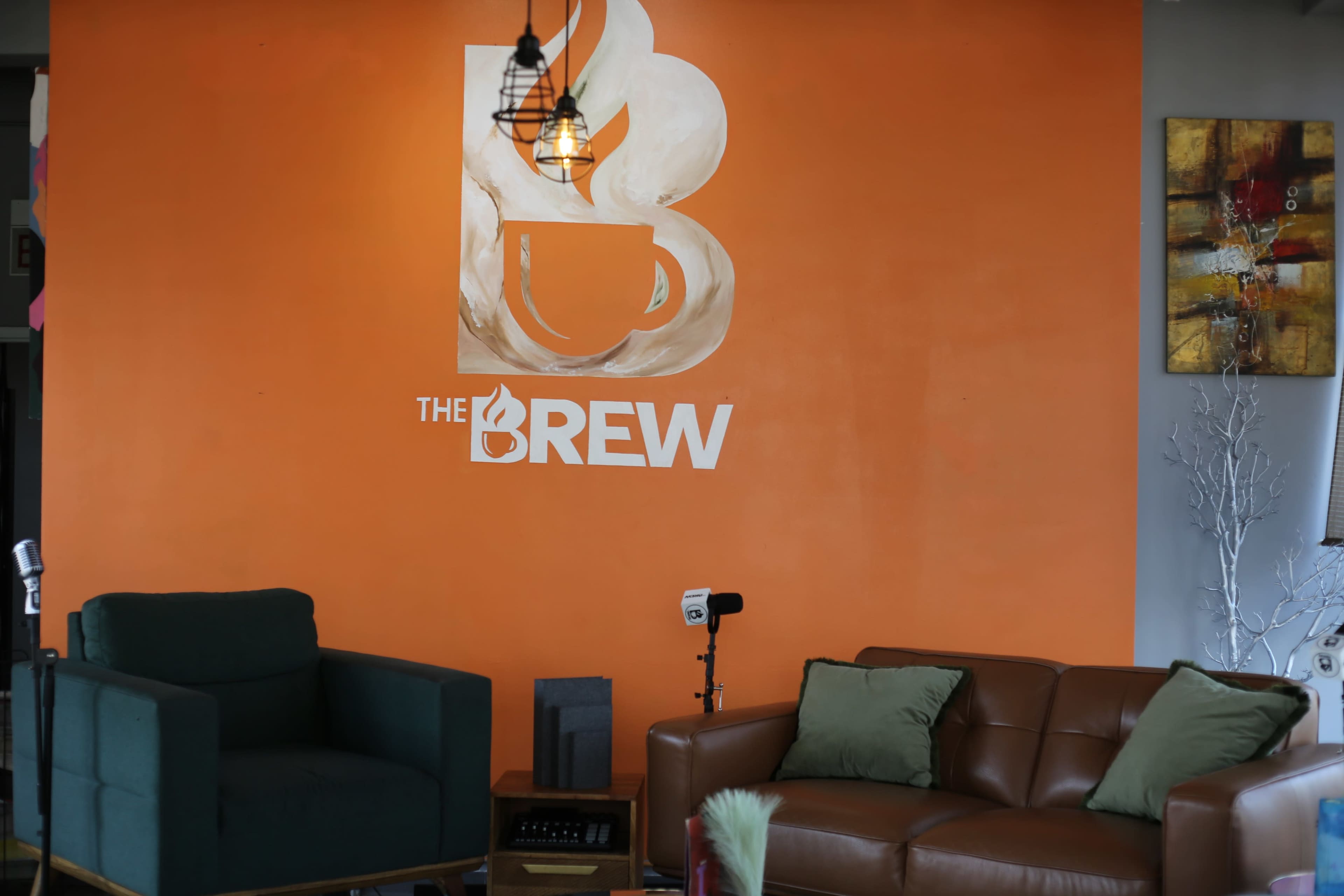 The image shows a cozy seating area in a café with an orange wall featuring the logo of "The Brew" and two different chairs in front of it.