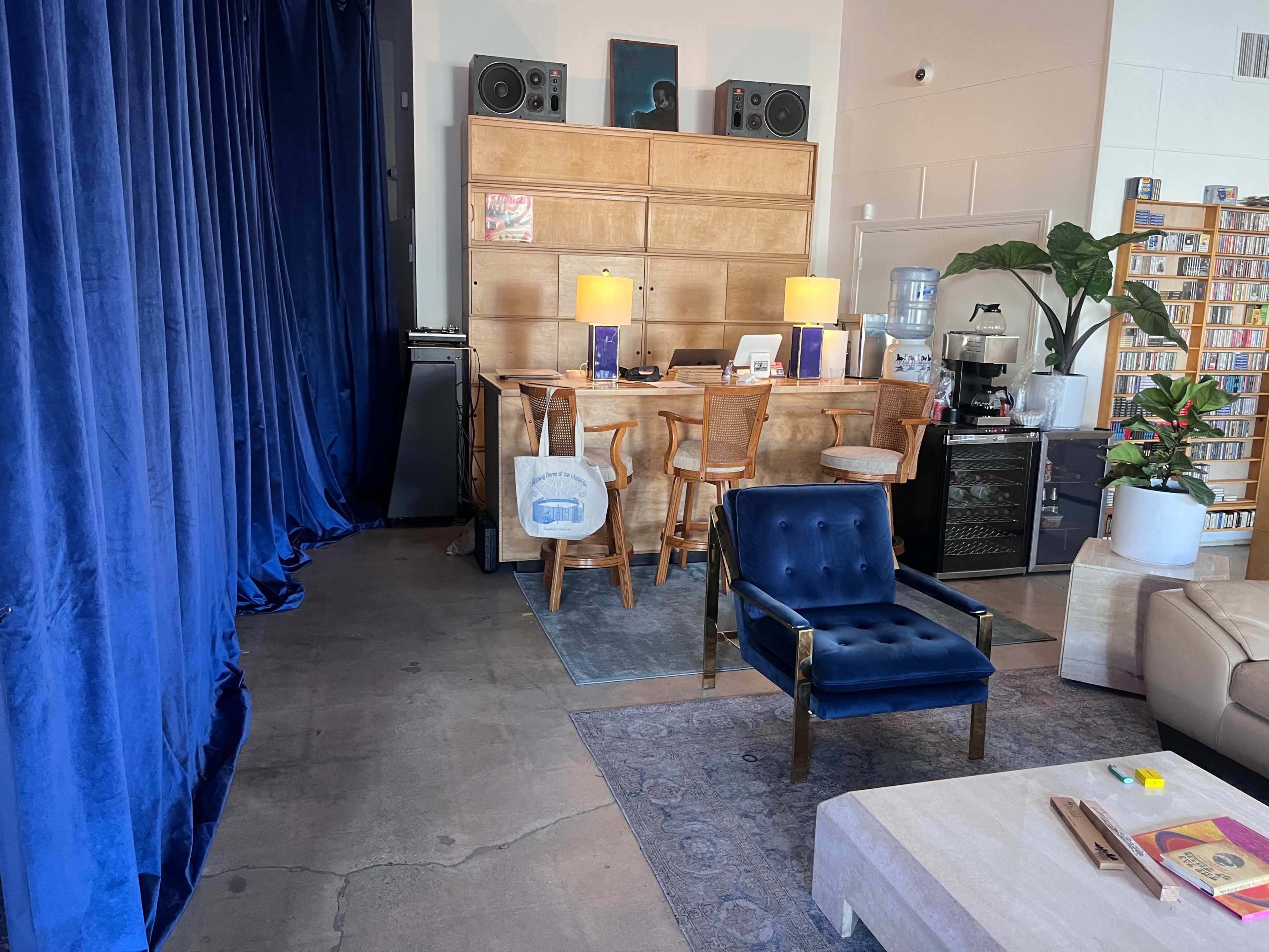 A cozy interior space featuring a wooden bar, blue curtains, and a seating area with a blue chair and a coffee table.