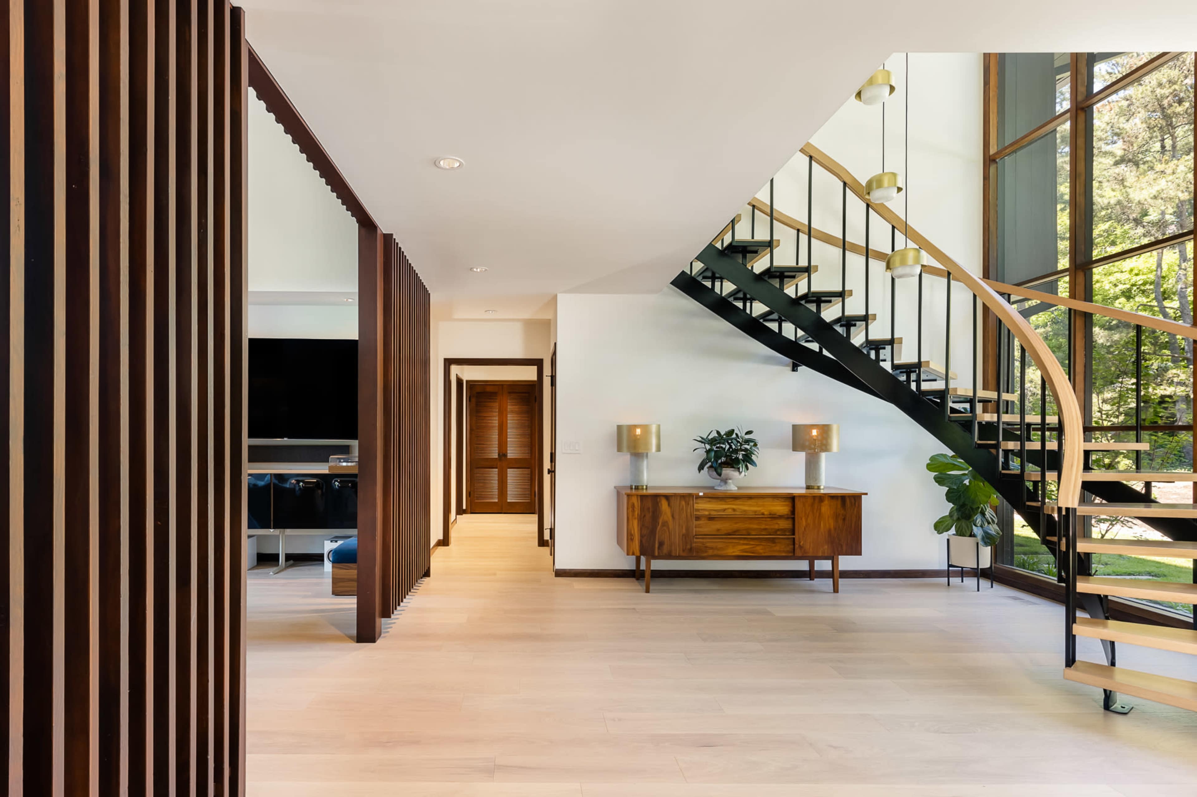 A modern interior featuring a spiral staircase, wooden accents, and a sideboard beside large windows.
