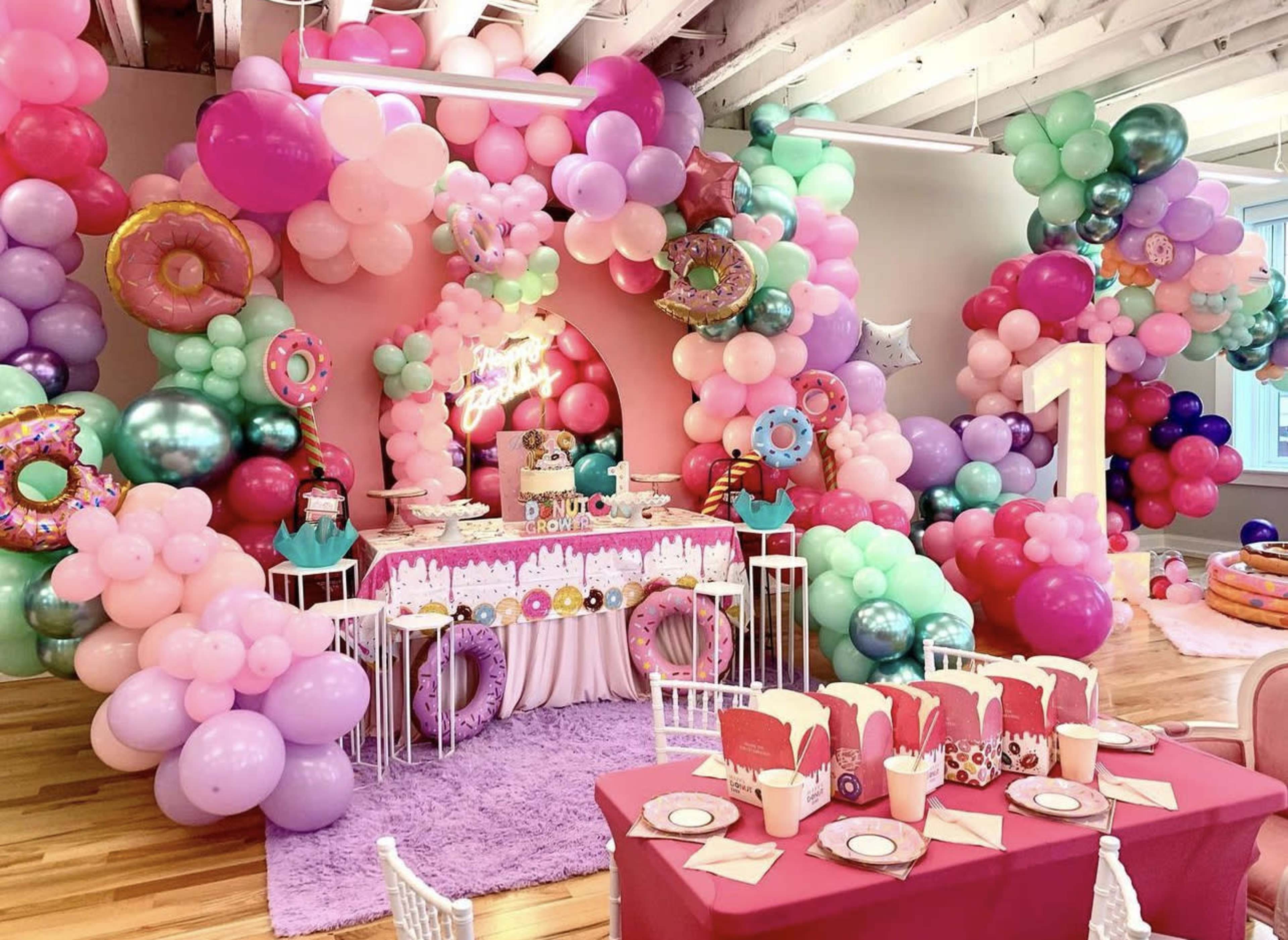 A colorful birthday party setup with a table adorned with a cake and decorations surrounded by balloon displays in various colors and shapes.