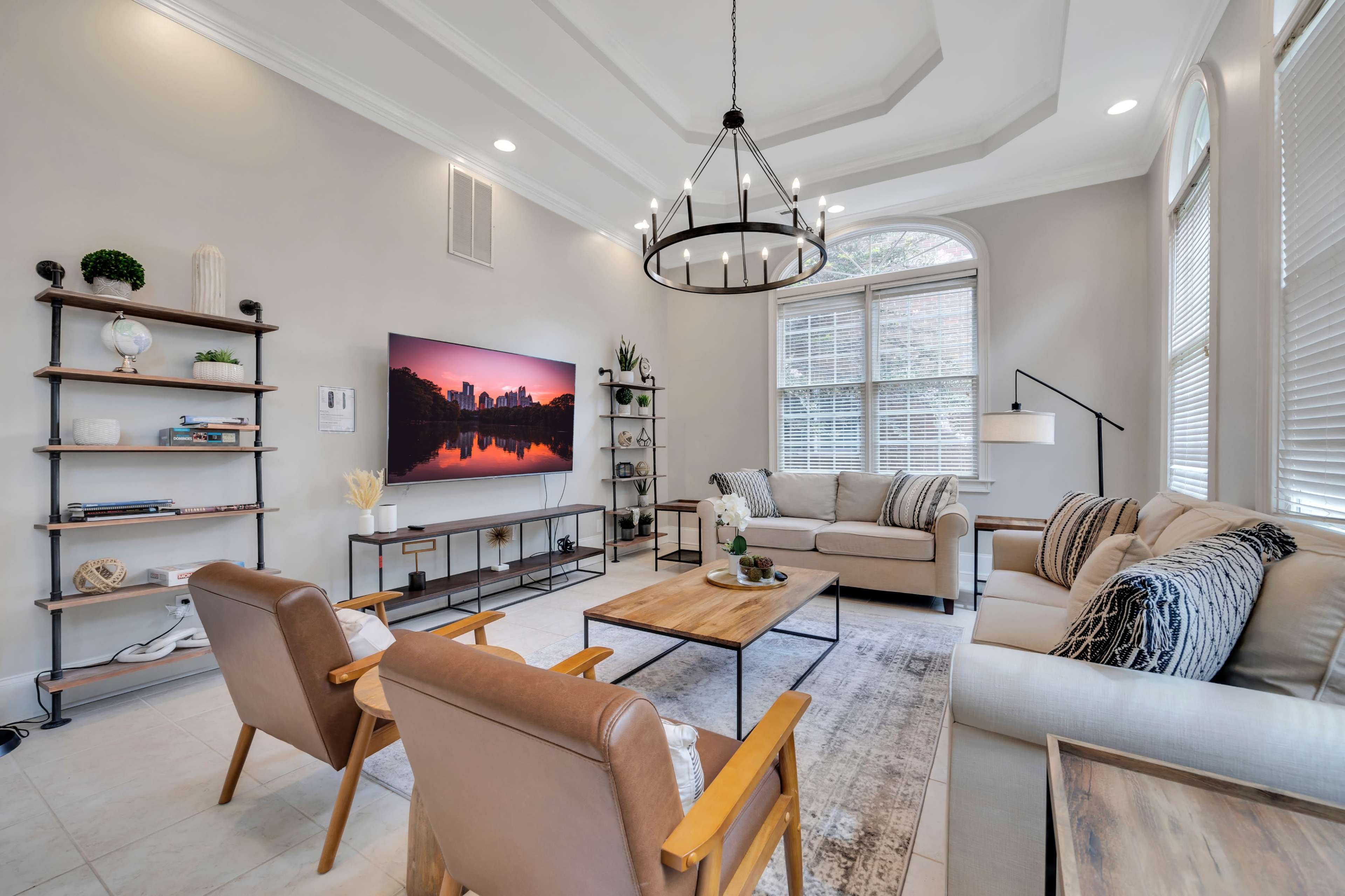 A modern living room with two brown armchairs, a light-colored sofa, a large television mounted on the wall, and a coffee table surrounded by decorative elements and plants.