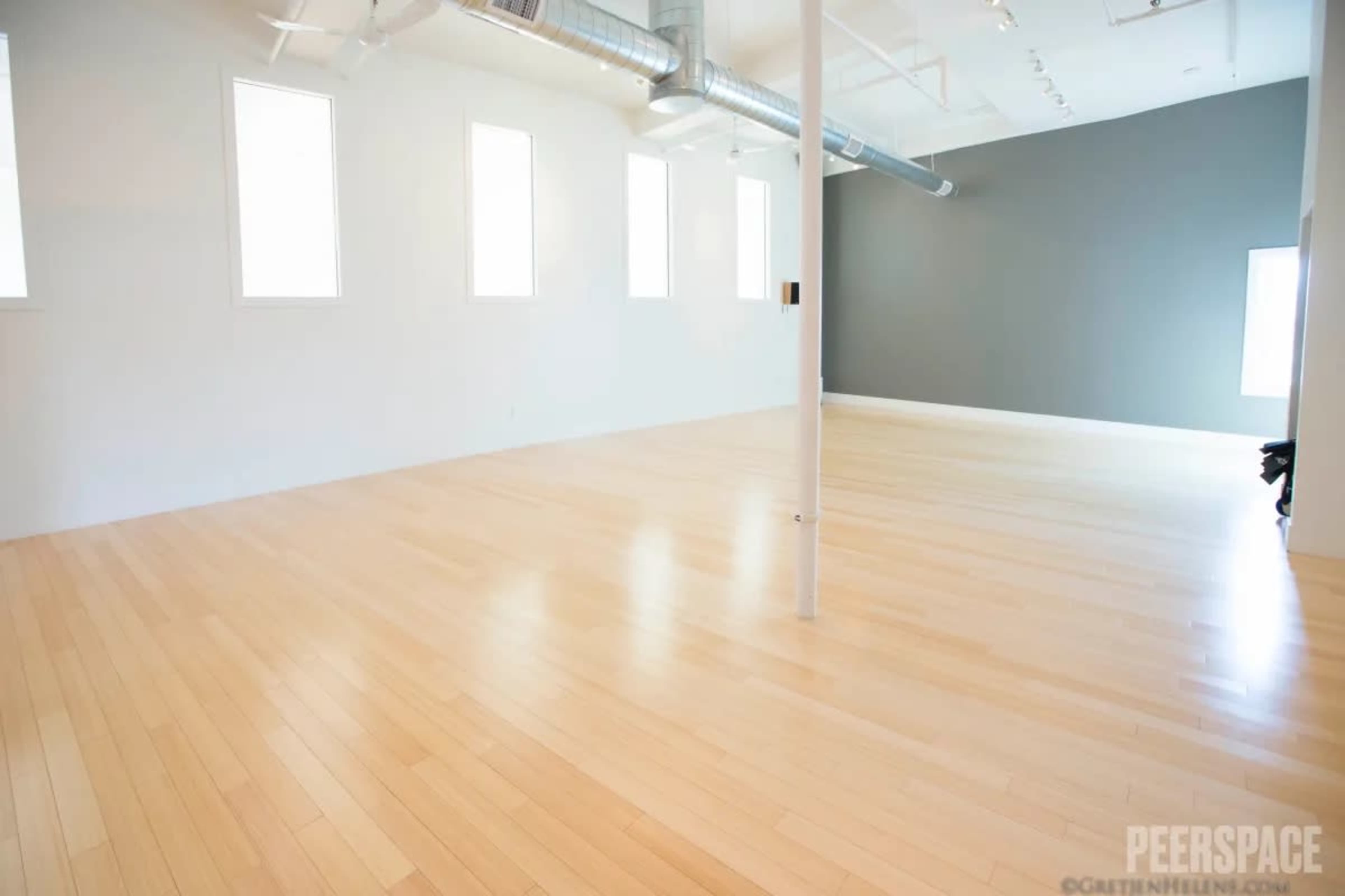 The image shows a spacious, minimalist room with hardwood floors, white walls, and a dark gray accent wall.