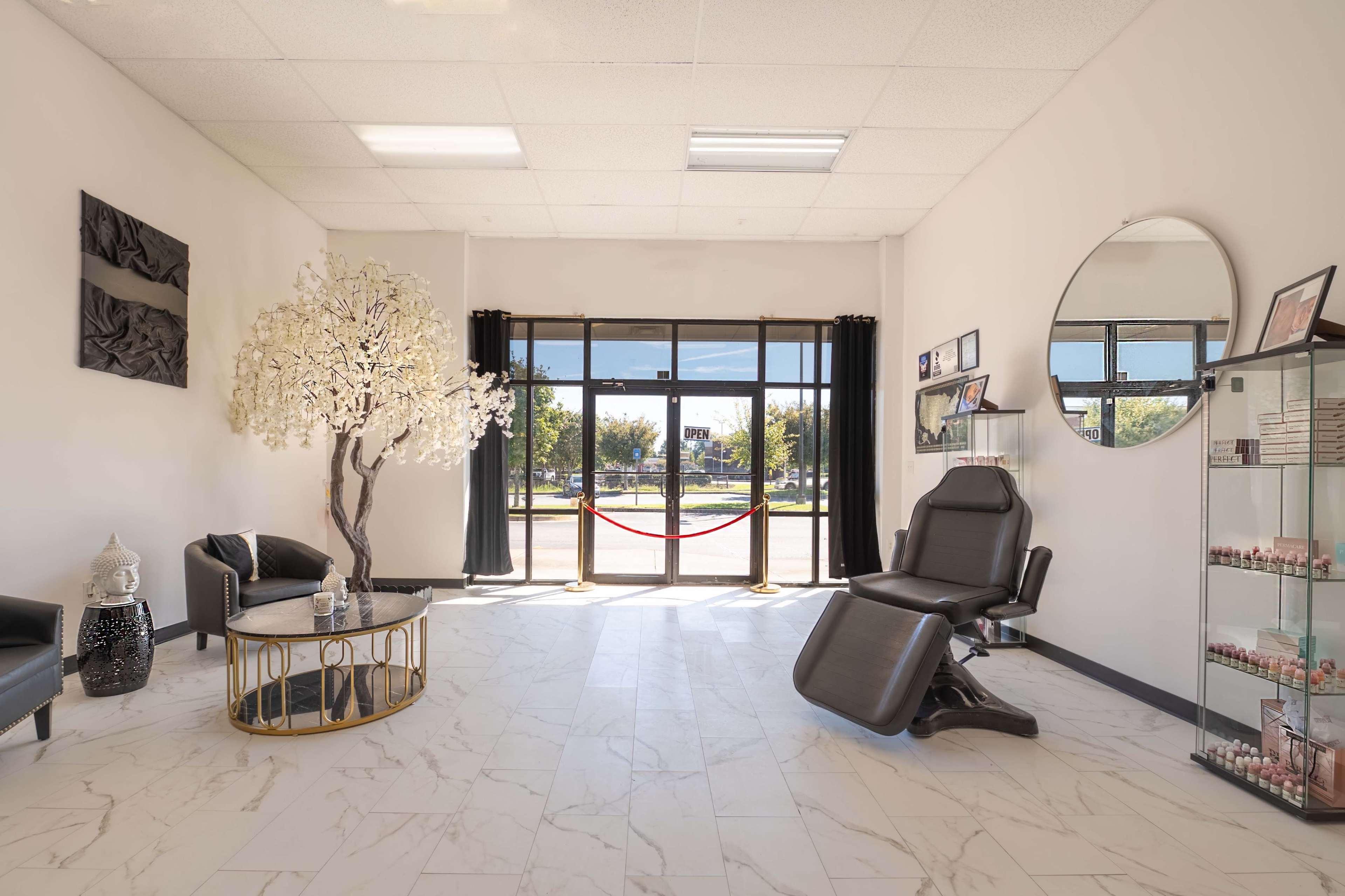 A modern interior of a salon with a large window, a decorative tree, and a black treatment chair.