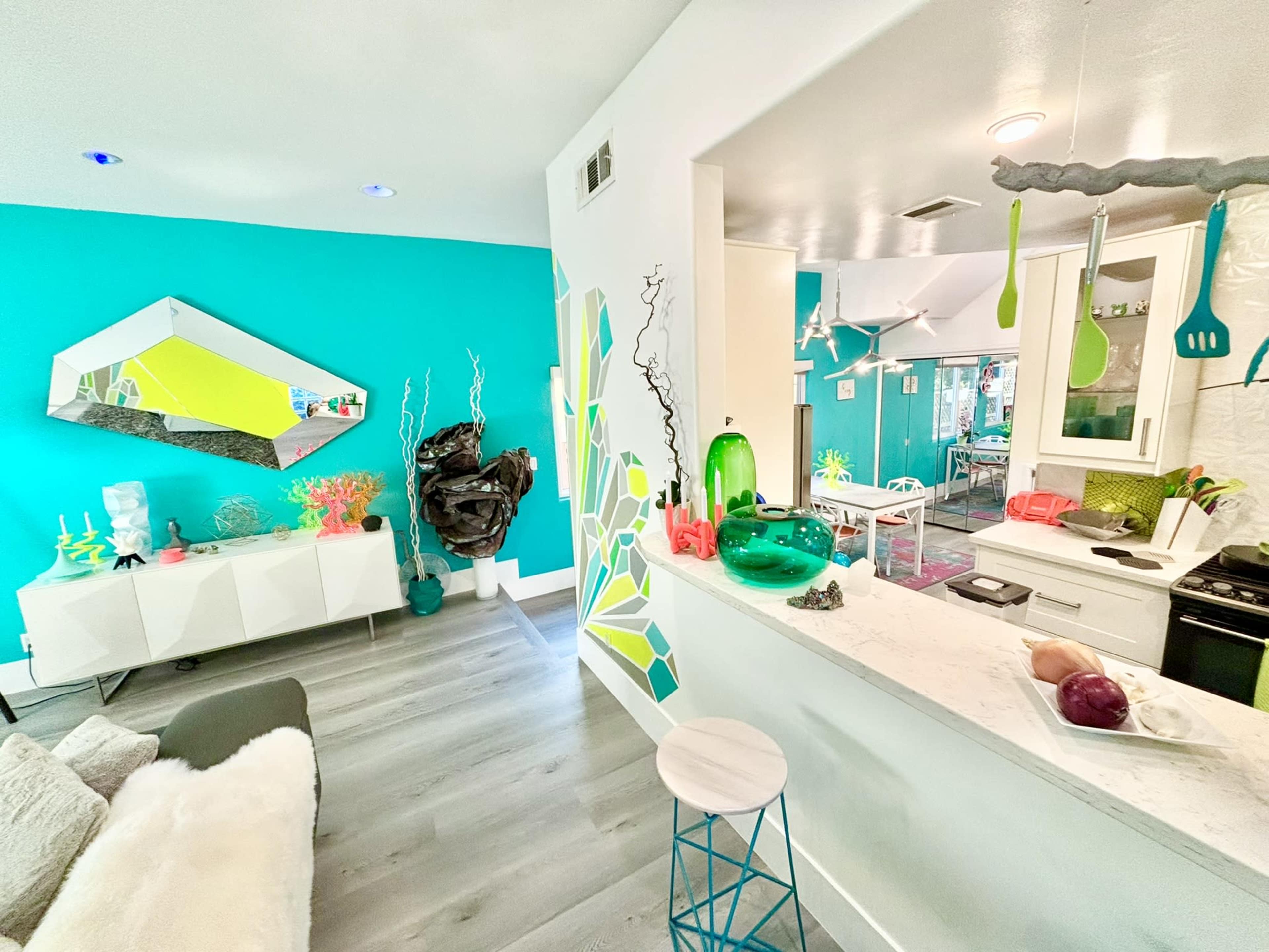 The image shows a brightly colored living space featuring turquoise walls, modern furniture, and a kitchen area with decorative elements in various shades of green.
