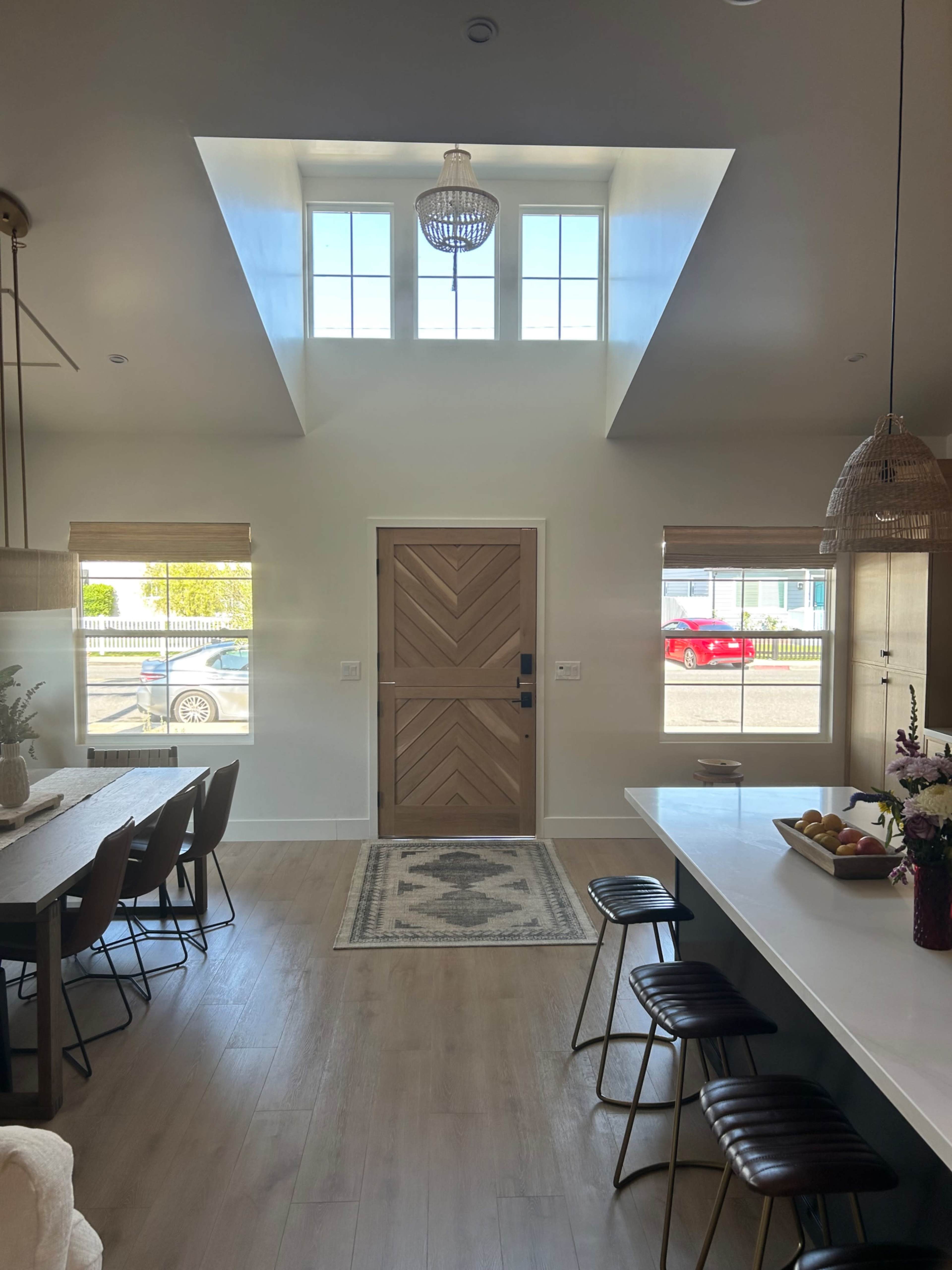 A modern interior features a large door at the center, framed by tall windows, with dining and seating areas on either side.