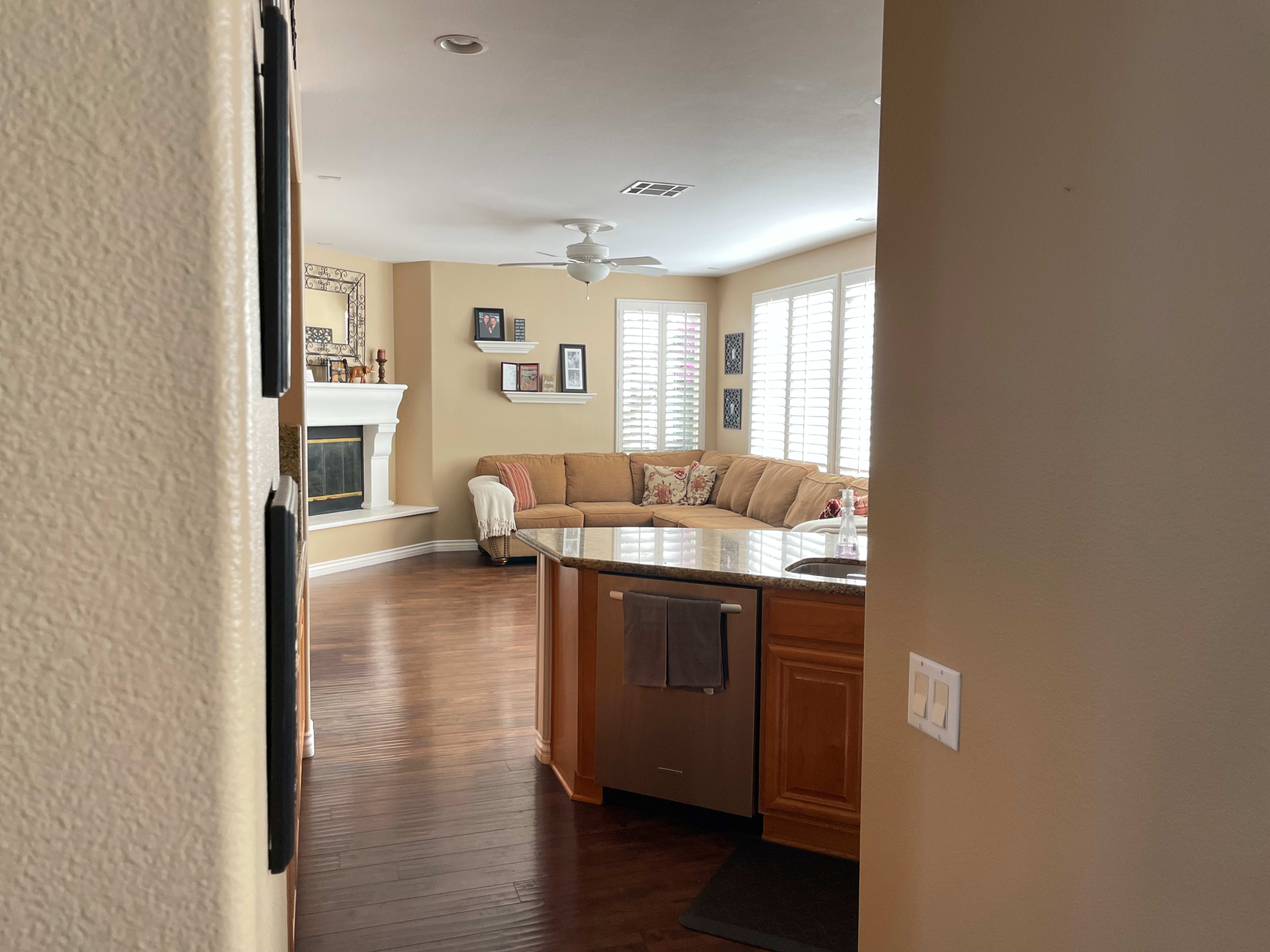 A view from a hallway into a living room featuring a sectional sofa, a fireplace, and a kitchen area with an island.