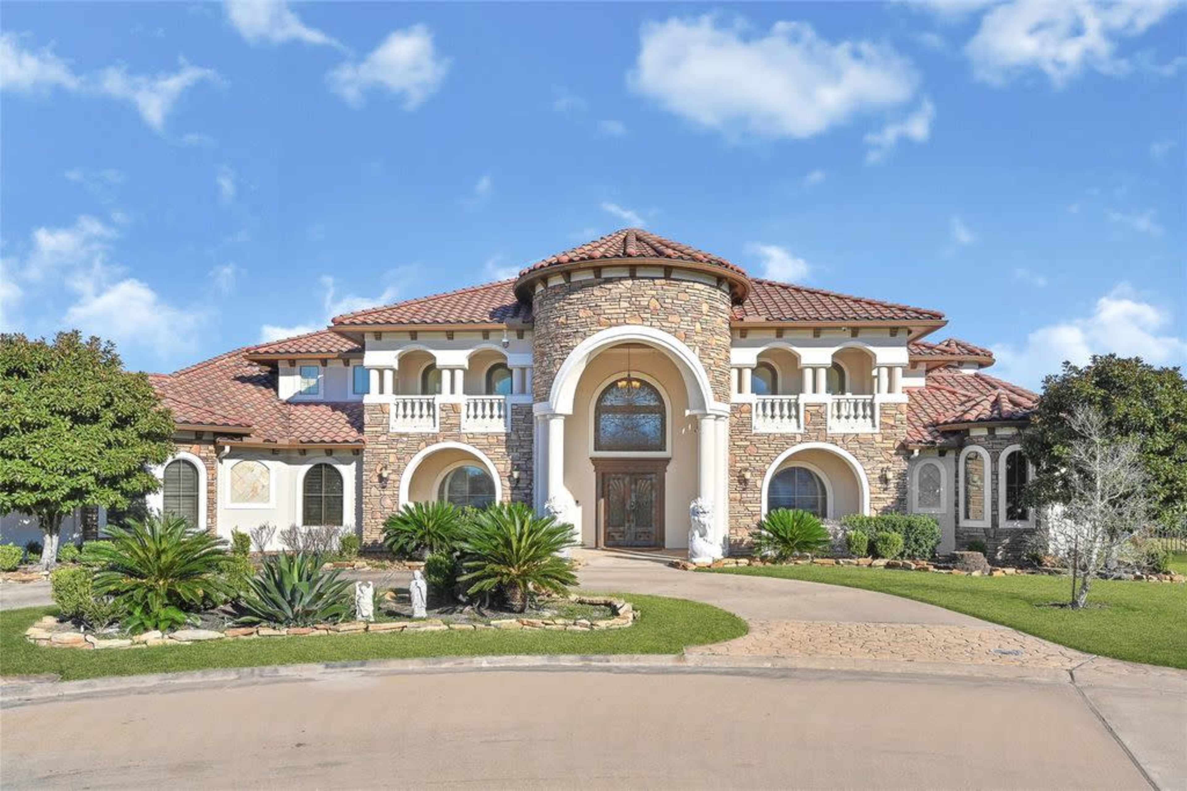 The image shows a large, multi-story residential house with a prominent circular entry and a tile roof, surrounded by landscaped greenery and a curved driveway.