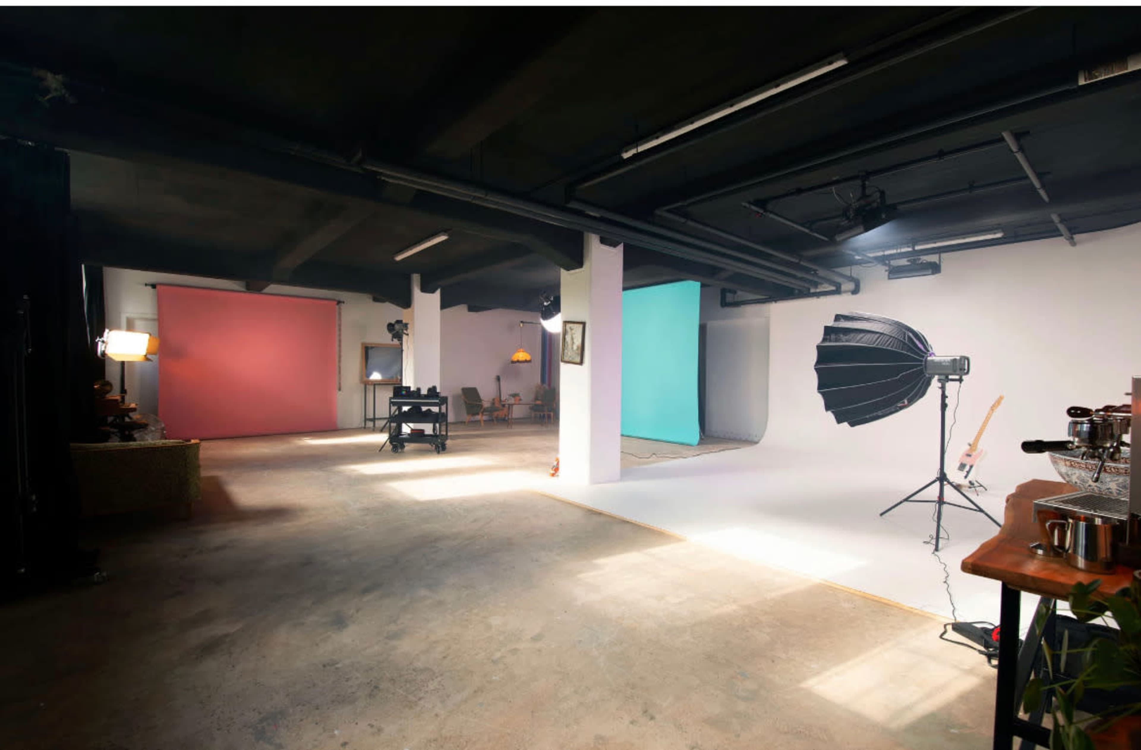 The image shows a photography studio with colorful backdrops, equipment on stands, and a spacious, uncluttered floor.