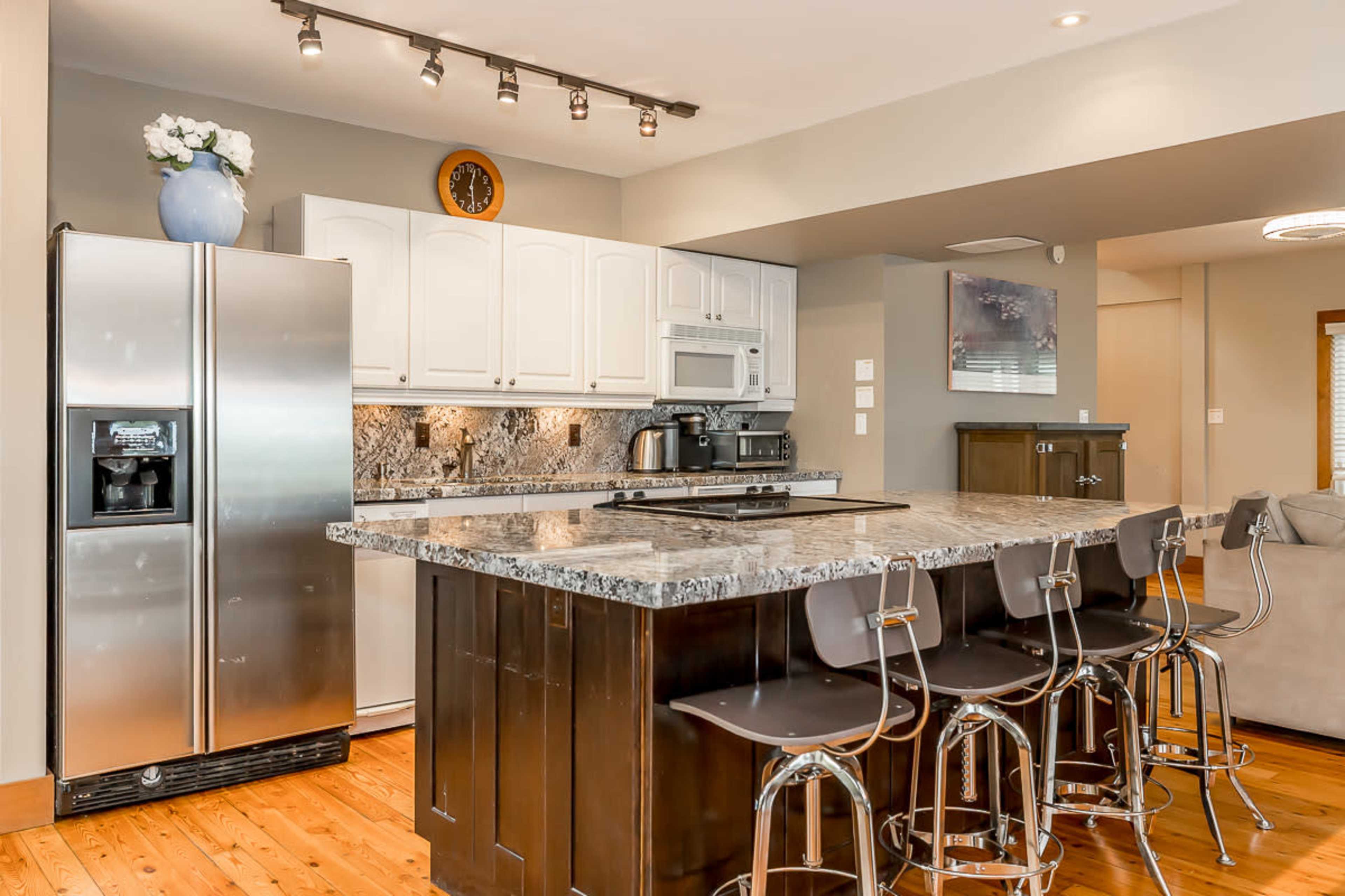 A modern kitchen with white cabinets, a large marble countertop, stainless steel appliances, and seating at the island.