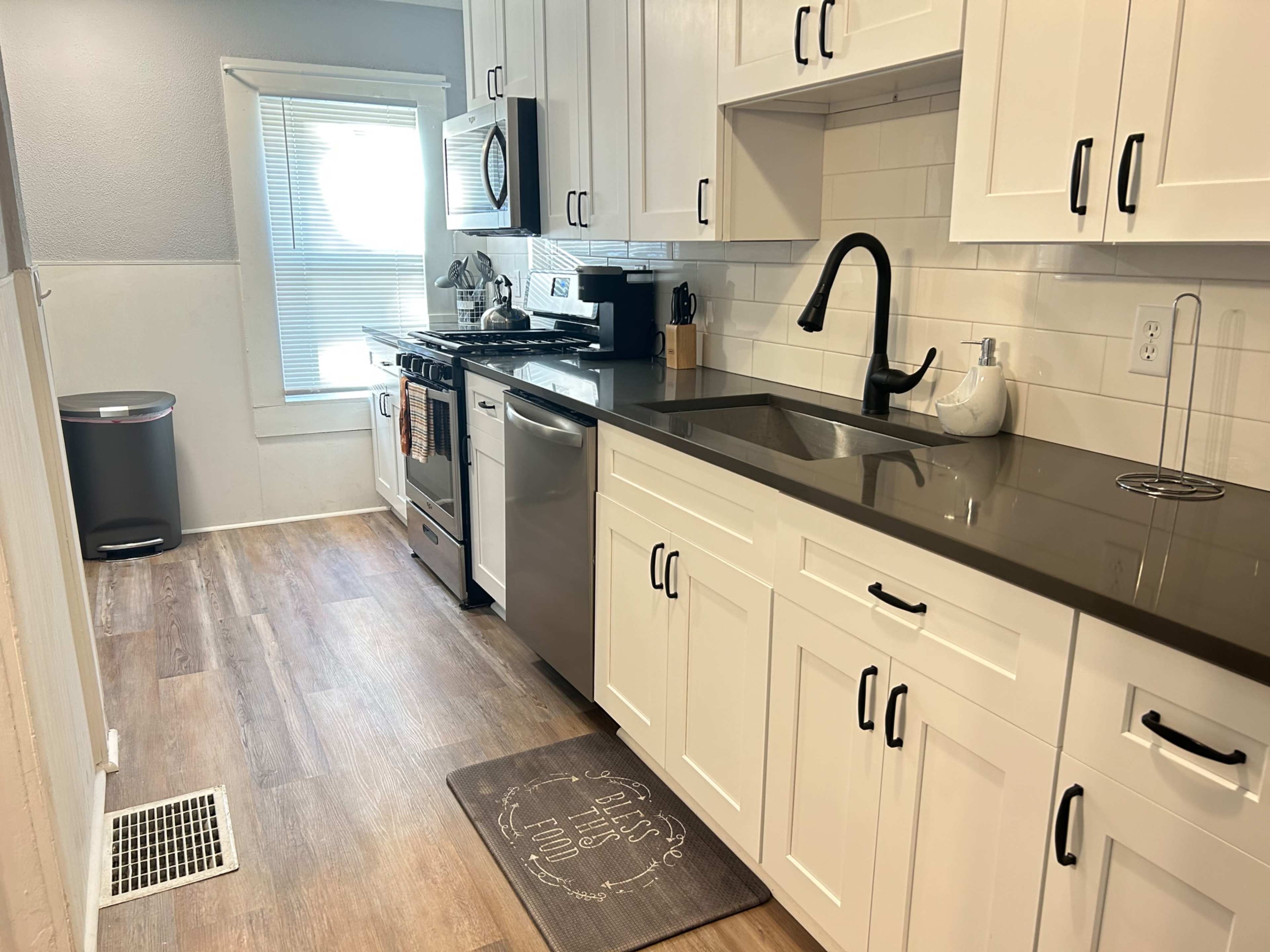 A modern kitchen featuring white cabinets, a stainless steel refrigerator, a black faucet, and a window with natural light illuminating the space.