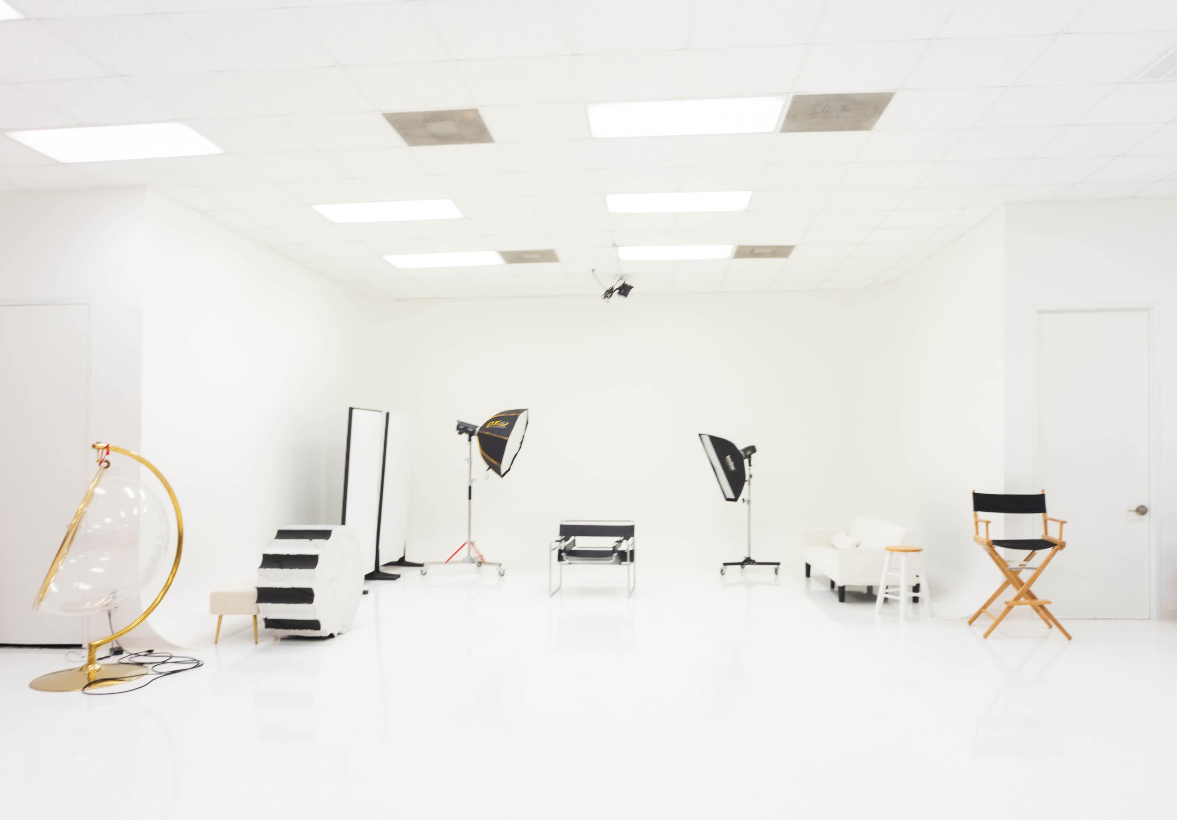 The image shows a bright, empty studio space equipped with photography lighting, a seating area, and a large mirror.