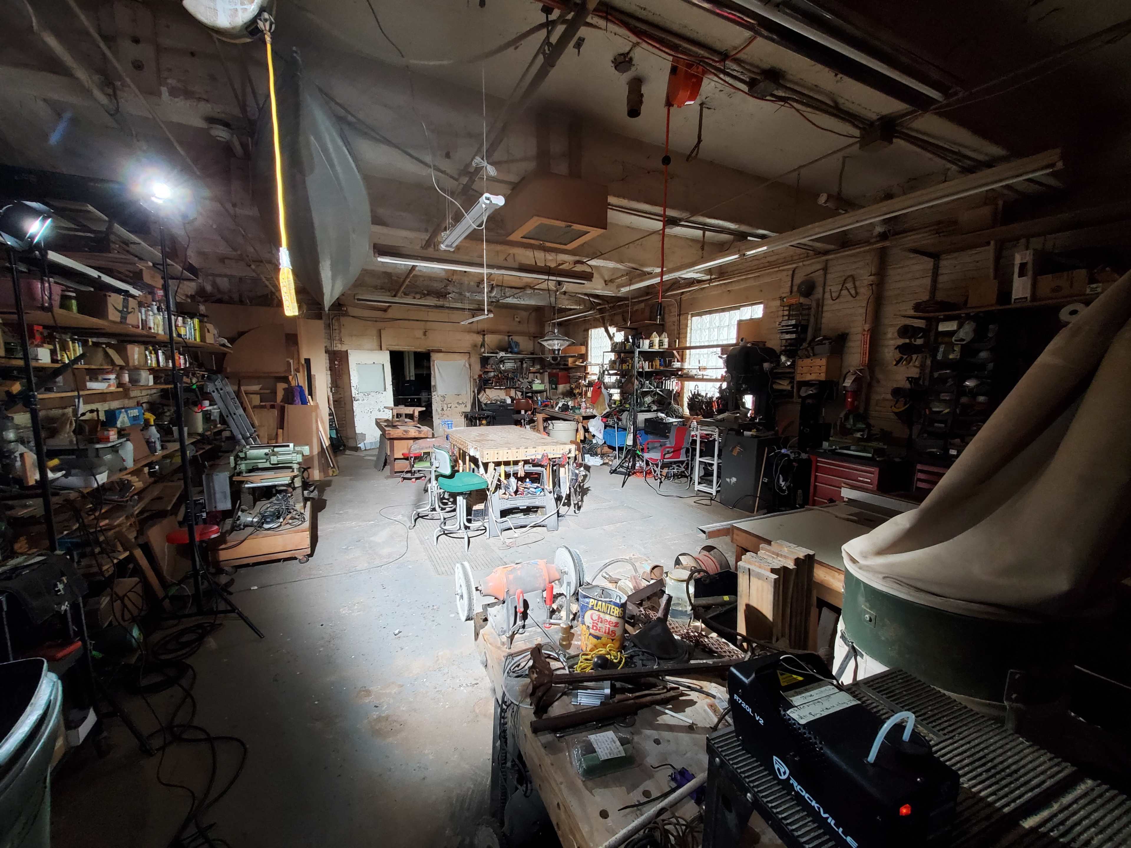 A cluttered workshop filled with various tools, equipment, and workstations under overhead lighting.