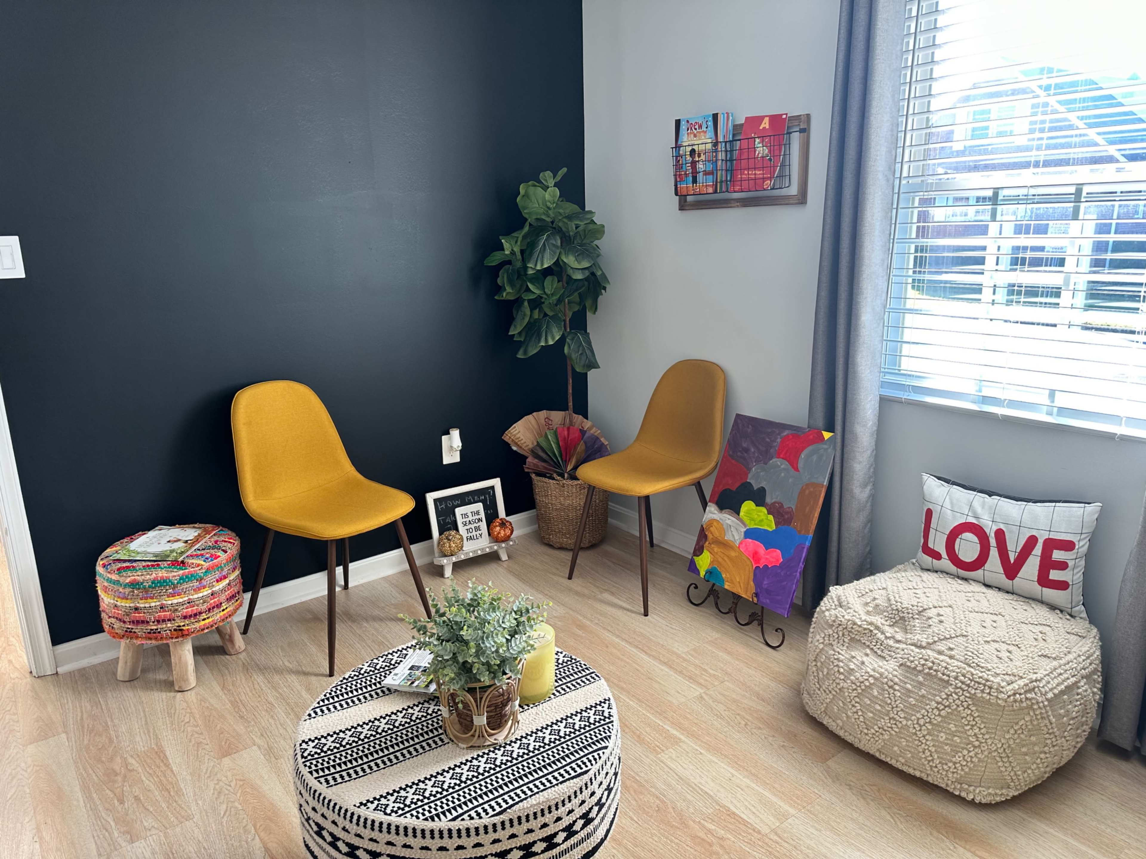 A cozy corner of a room featuring two yellow chairs, a small round table, a potted plant, colorful artwork, and decorative pillows.
