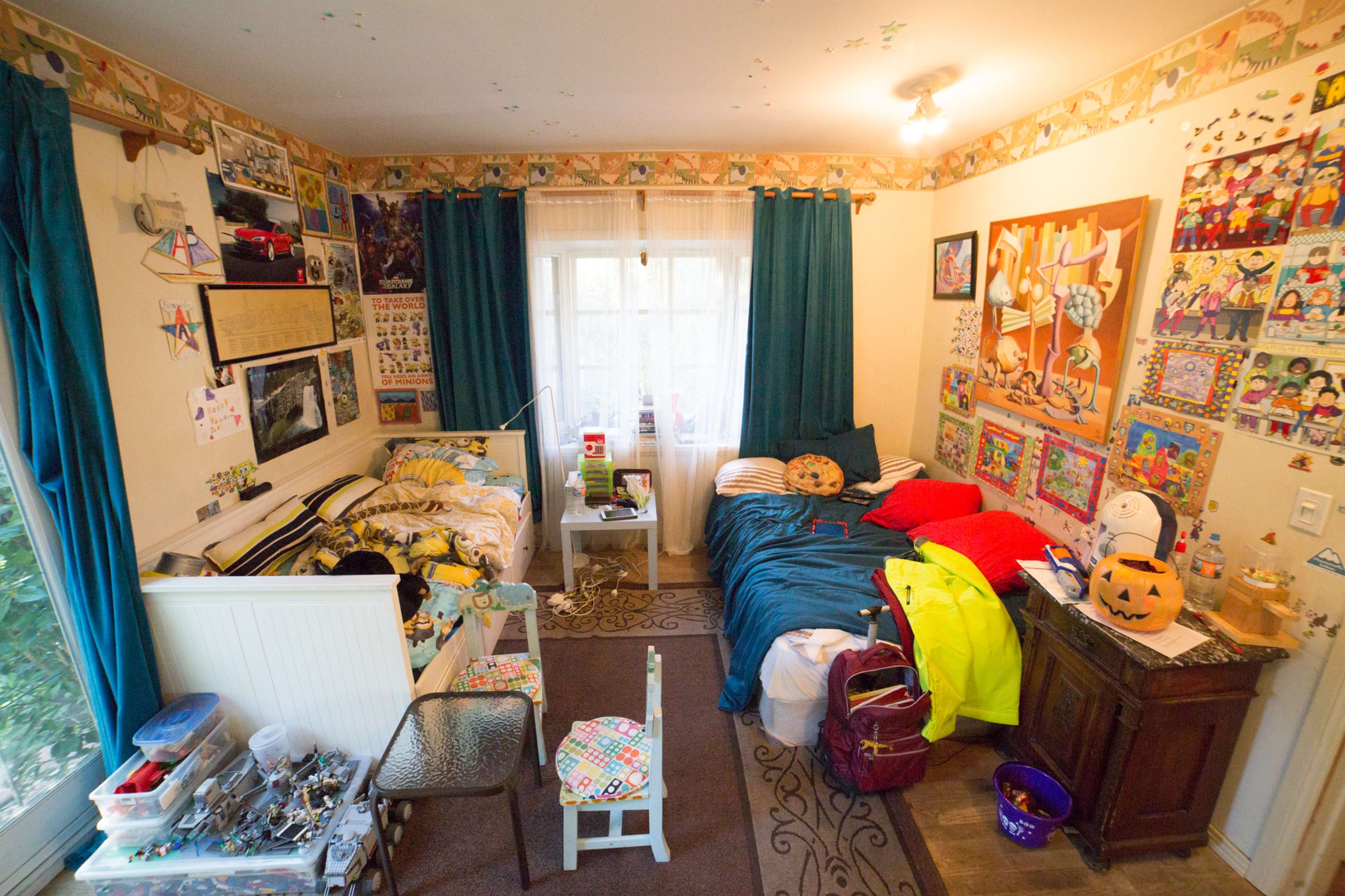 The image shows a colorful children's bedroom with two beds, various toys, and decorated walls filled with drawings and posters.