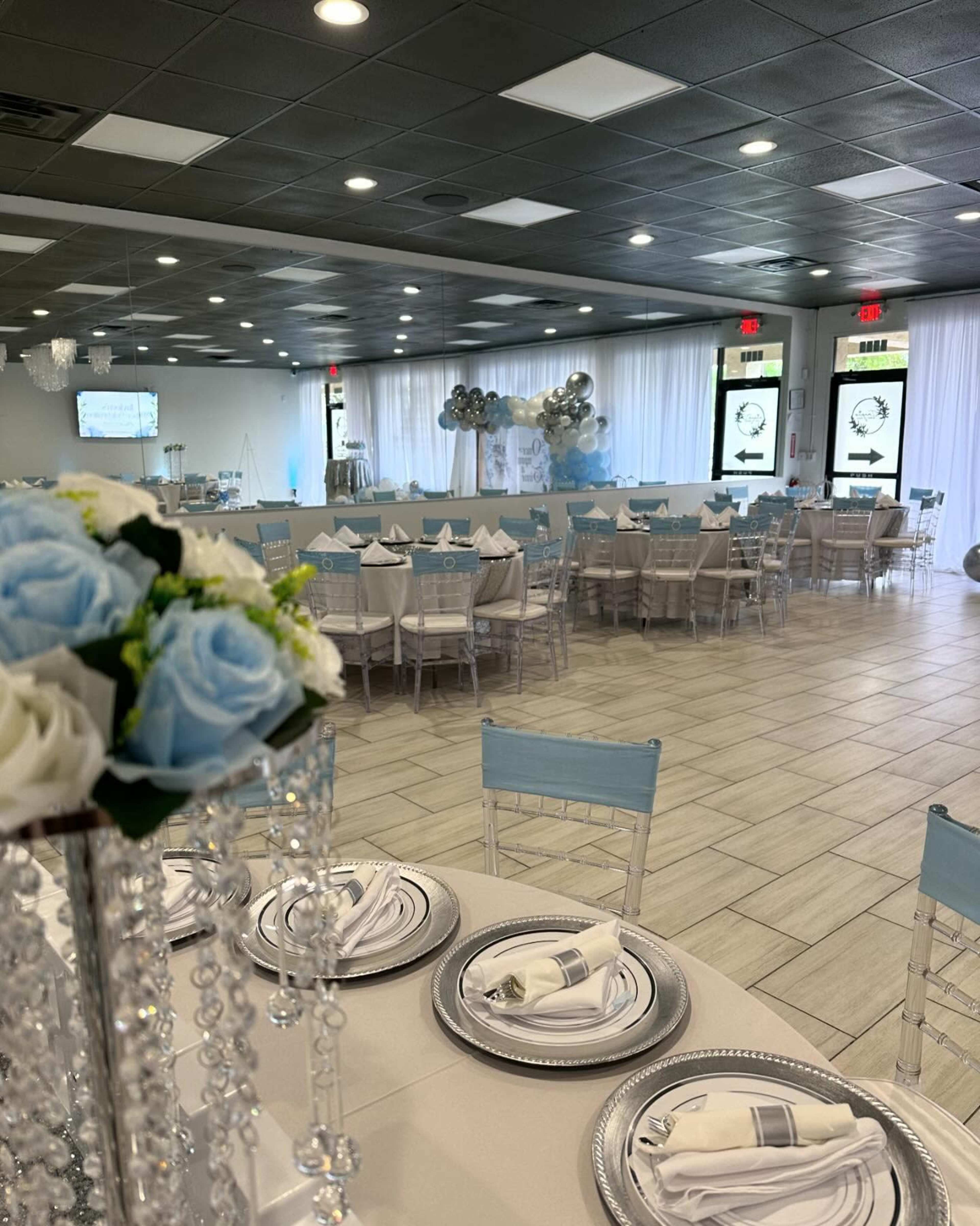 The image shows a decorated event space with tables set for a gathering, featuring light blue accents and floral centerpieces.