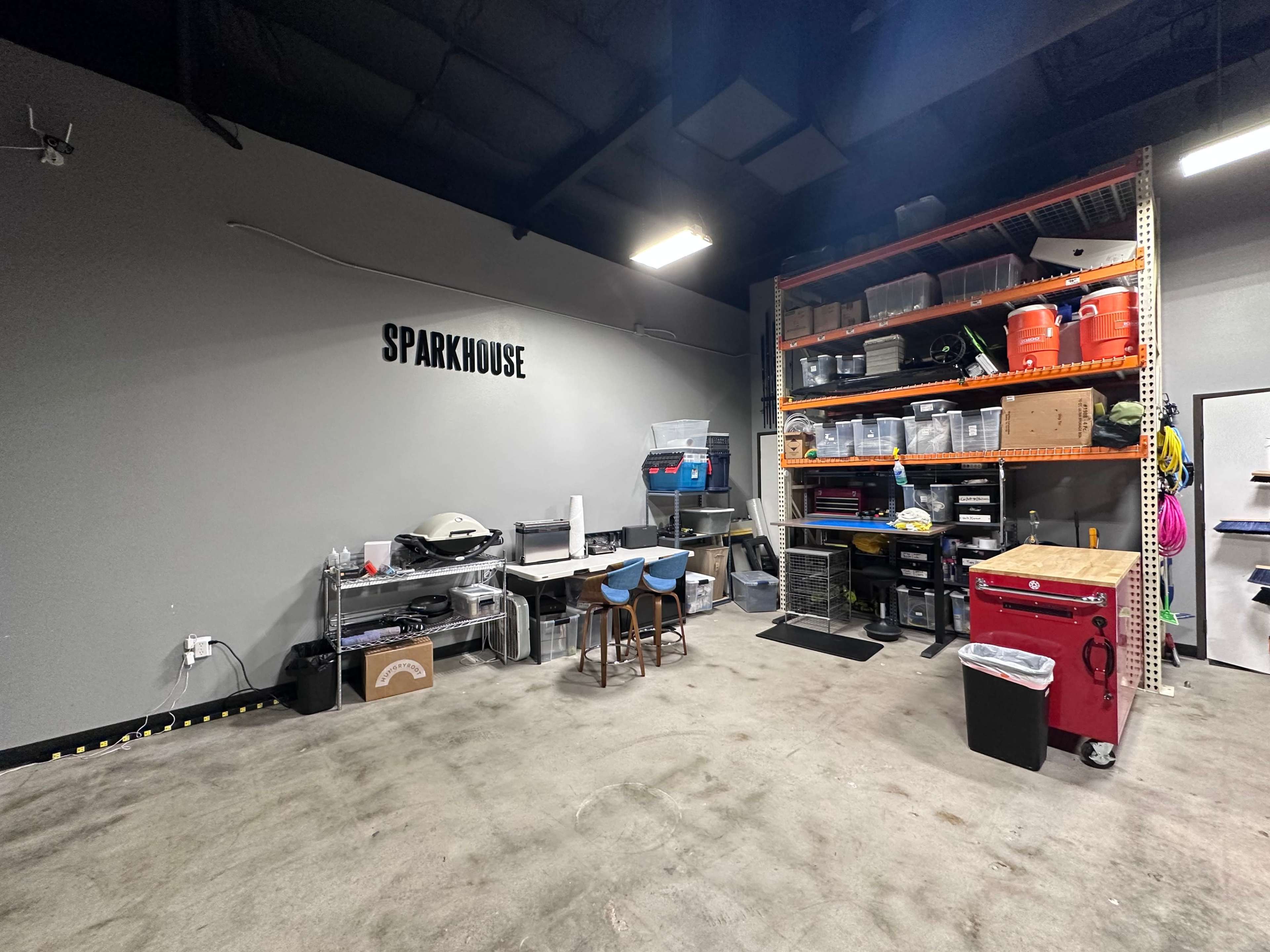 A spacious garage or workshop area with shelves filled with storage bins, tools, and a workspace equipped with stools and various supplies.