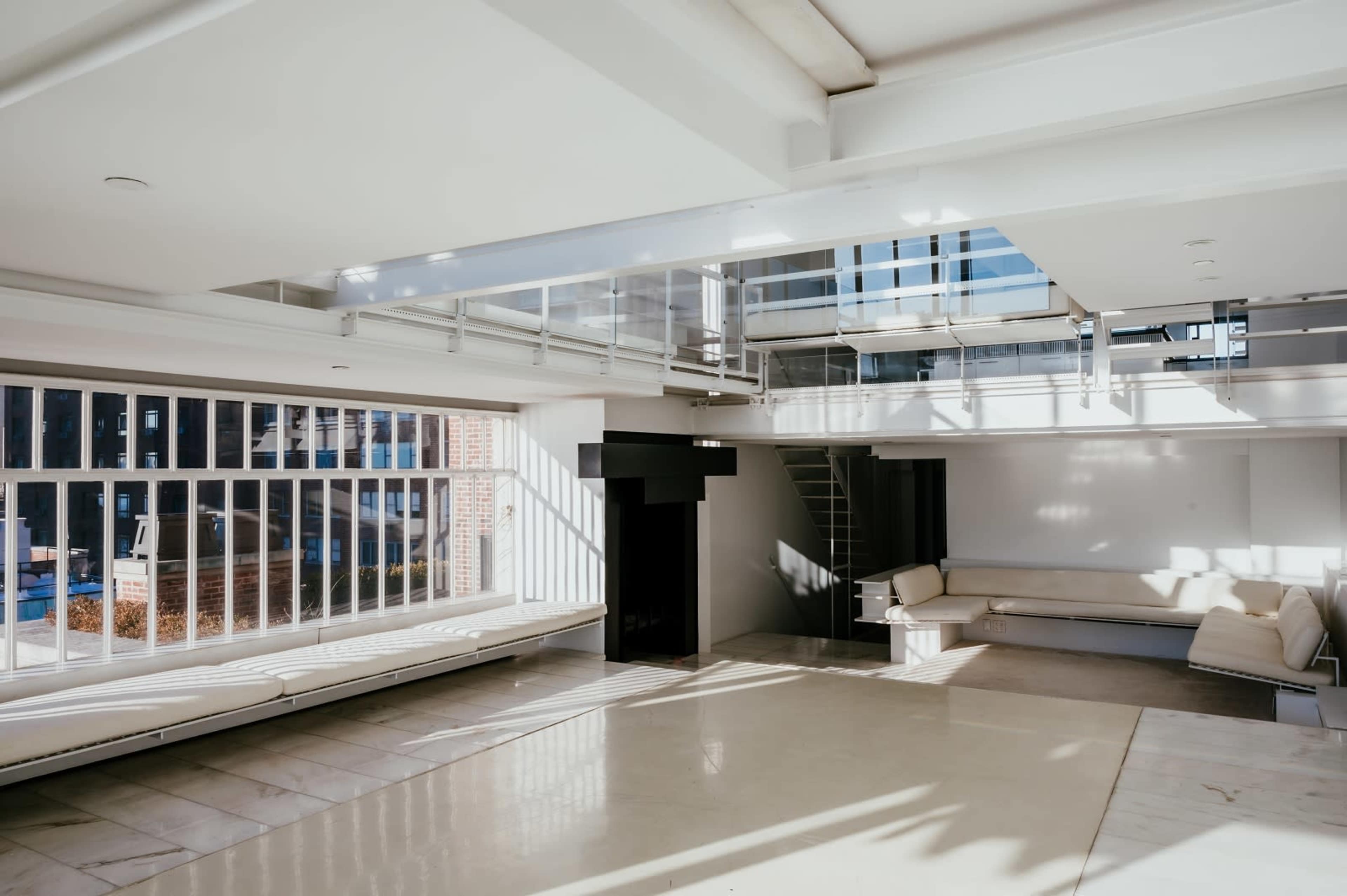 The image shows a spacious, modern interior with large windows, white walls, and minimalist furniture.