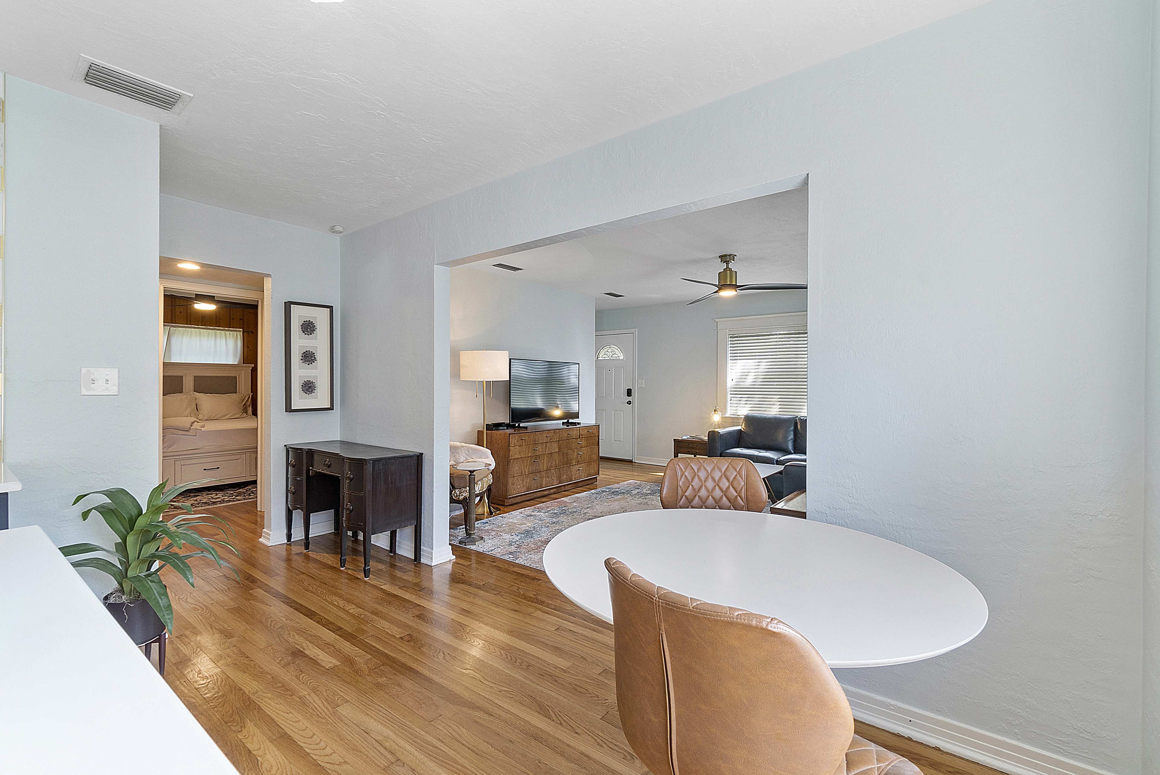 An open living area with hardwood floors, a round dining table, and a view into a bedroom through an archway.