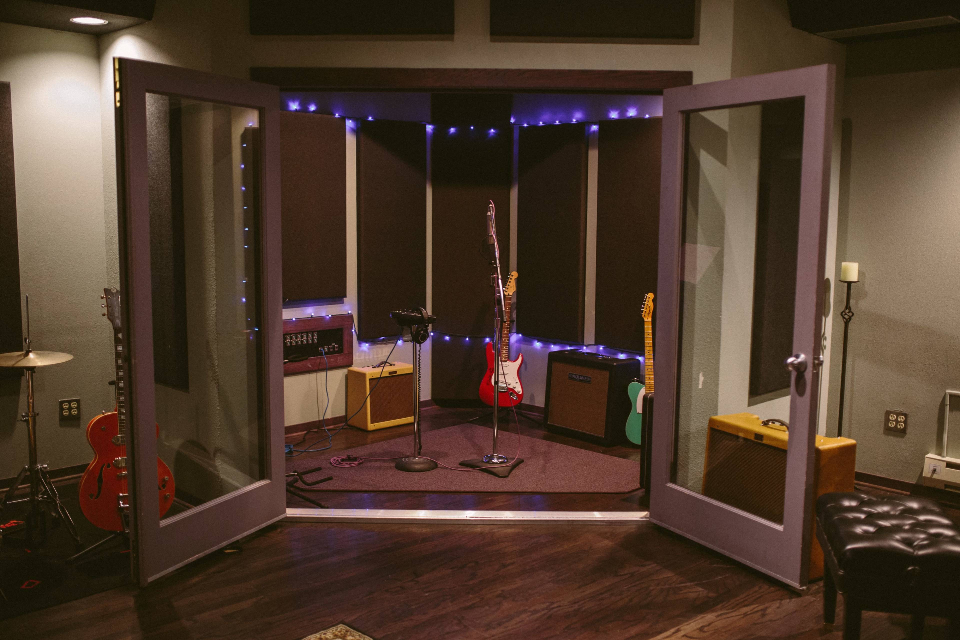 A music recording studio features an array of guitars, amplifiers, and a microphone set up in the center, illuminated by soft lights.