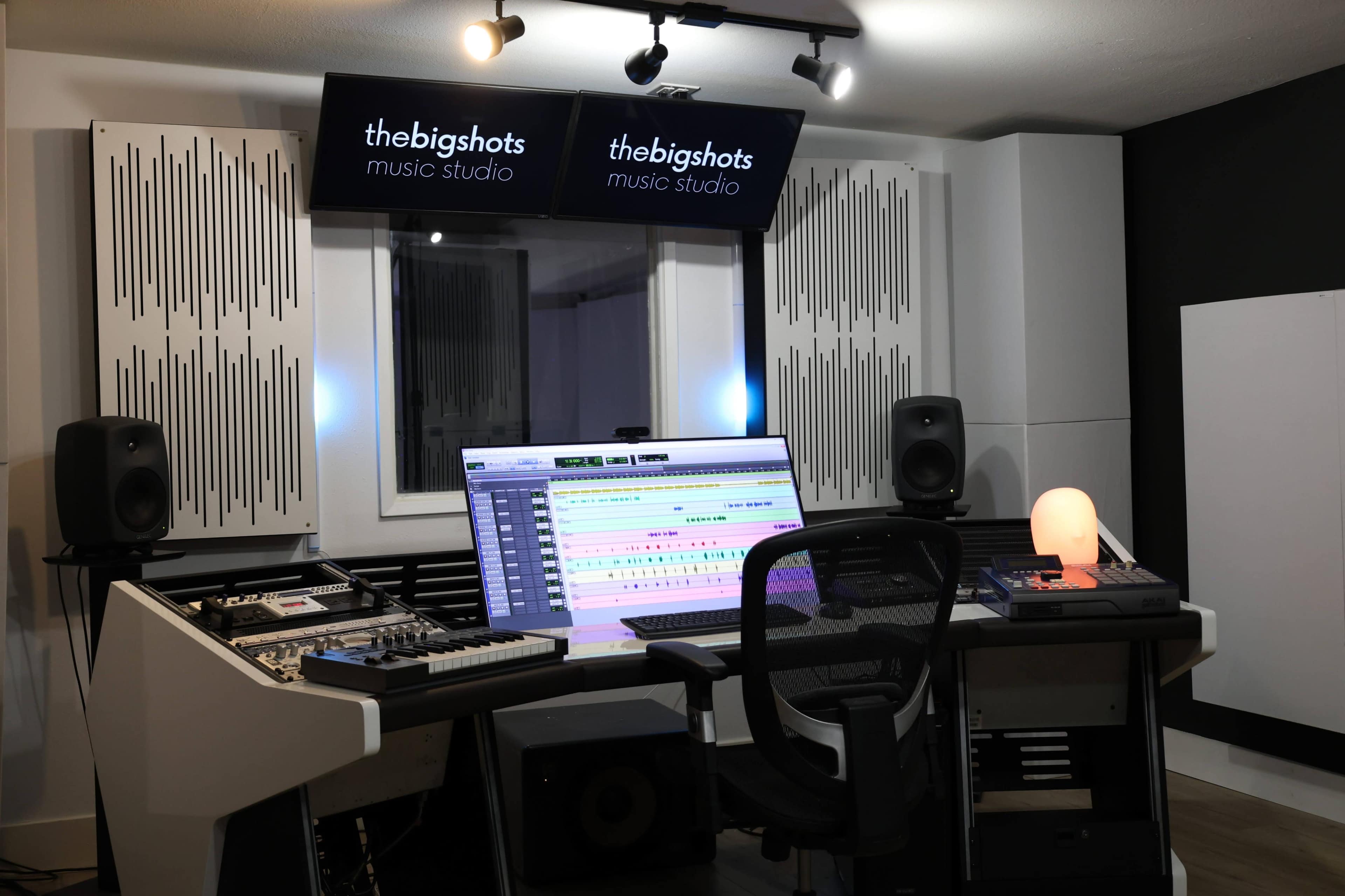 The image shows a music studio equipped with a large monitor, audio mixing equipment, and soundproof paneling.