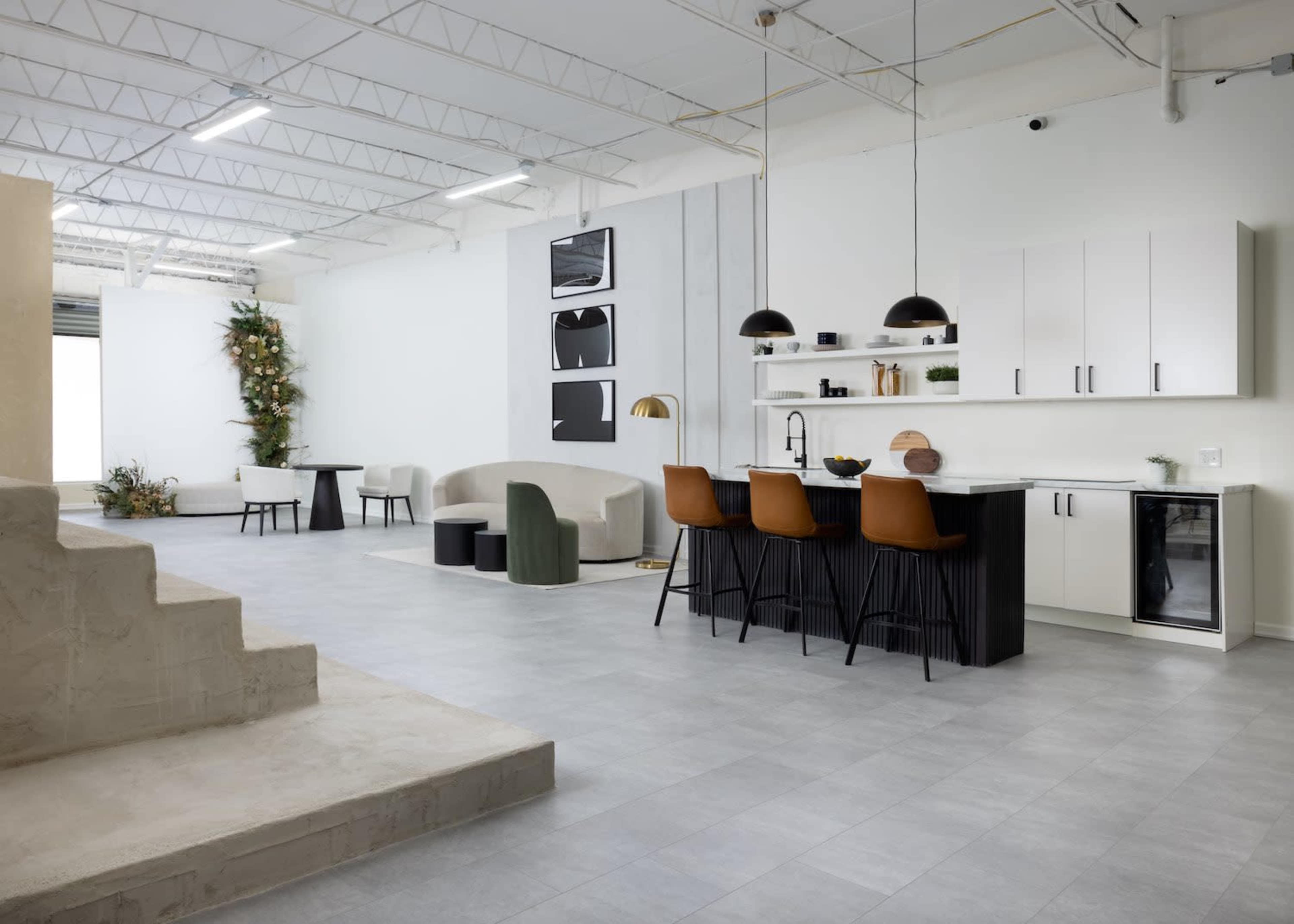 A modern open-concept living space featuring a kitchen with bar seating, a dining area, and minimalist furniture against a light-colored backdrop.