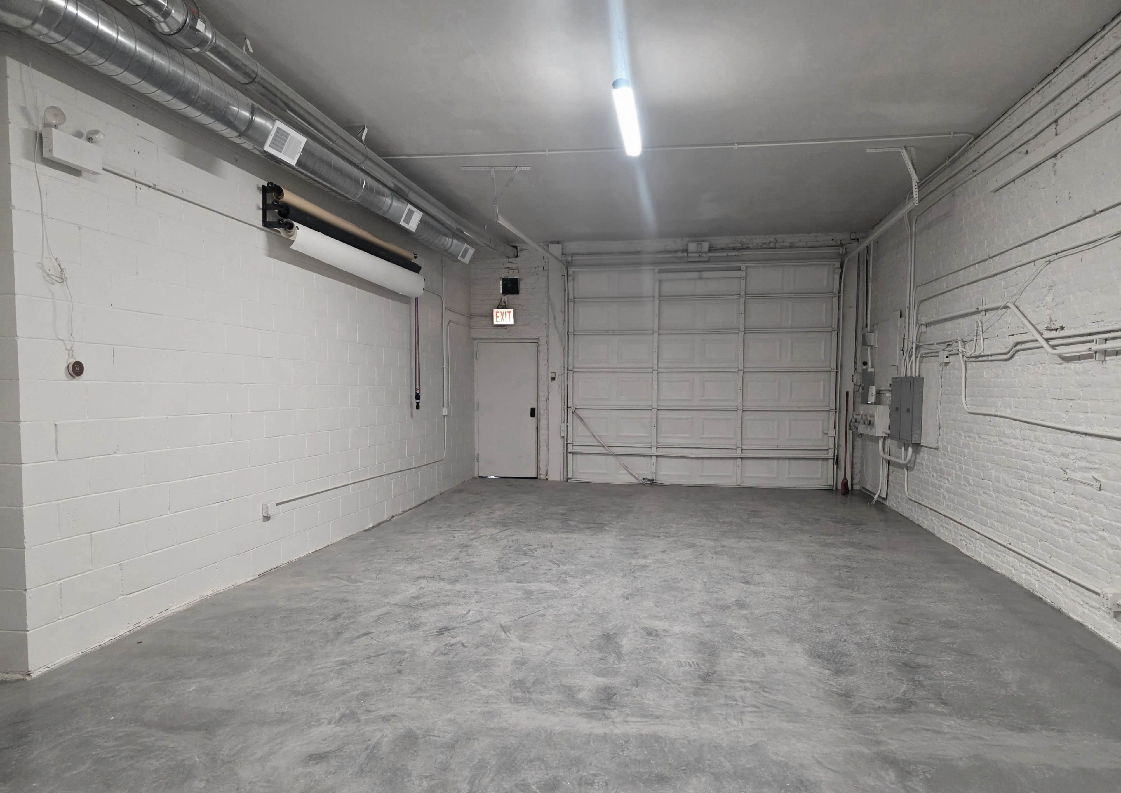 The image shows a spacious, empty garage with white walls, a concrete floor, and overhead lighting.