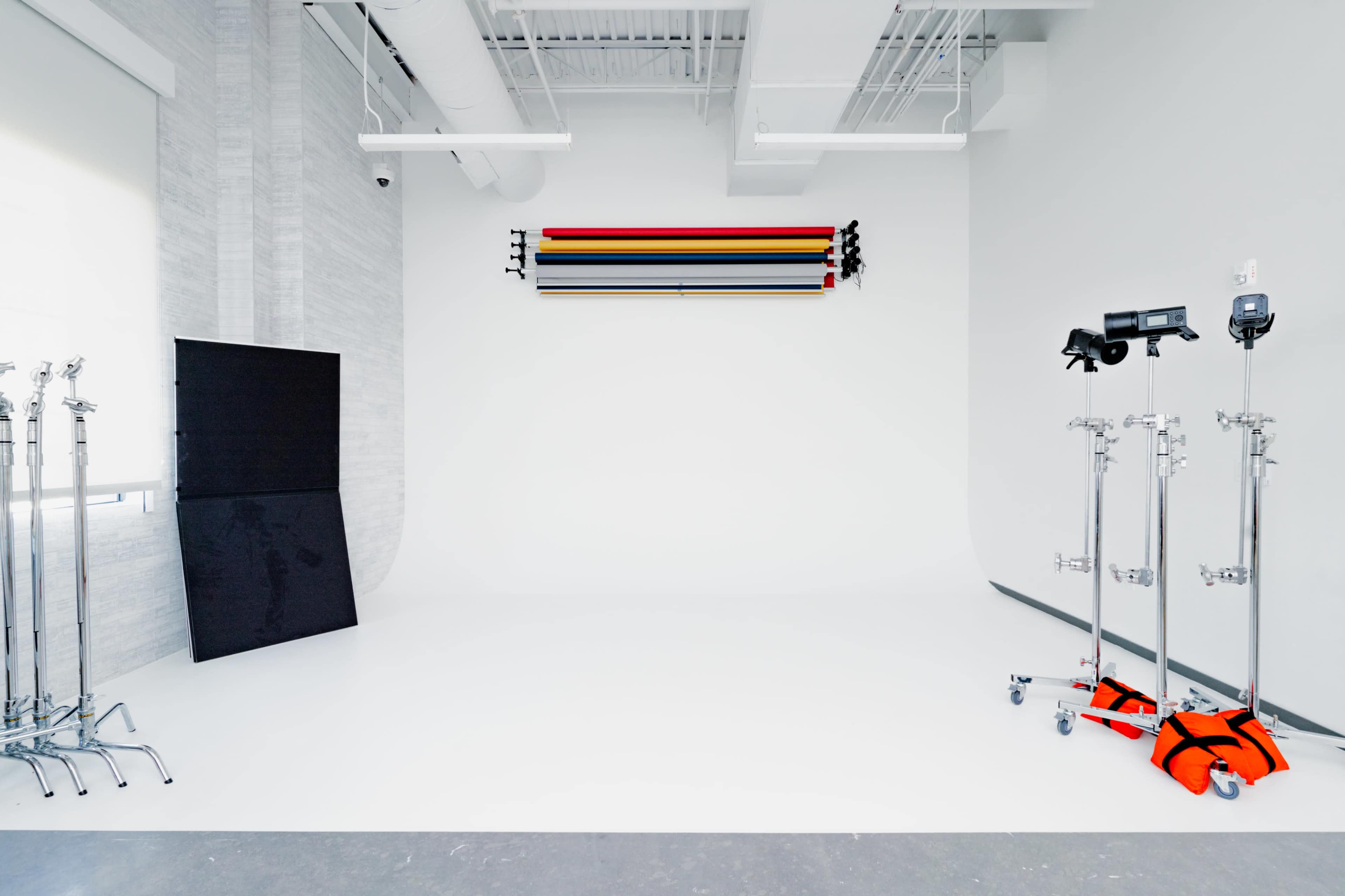 A photography studio with a white backdrop, colored background rolls on a rack, and lighting equipment on stands.
