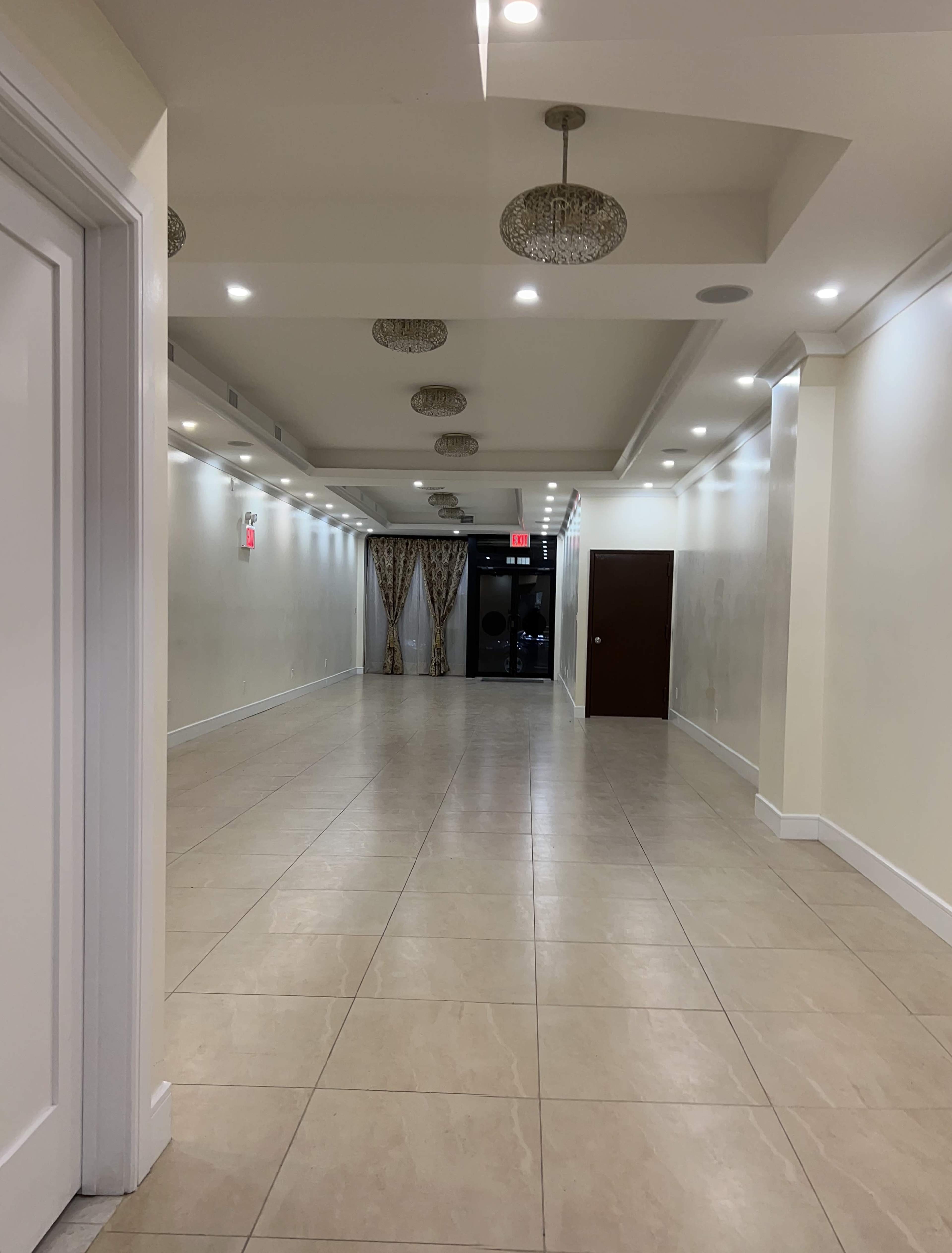 A well-lit hallway with tile flooring, decorative ceiling lights, and curtains at the far end.