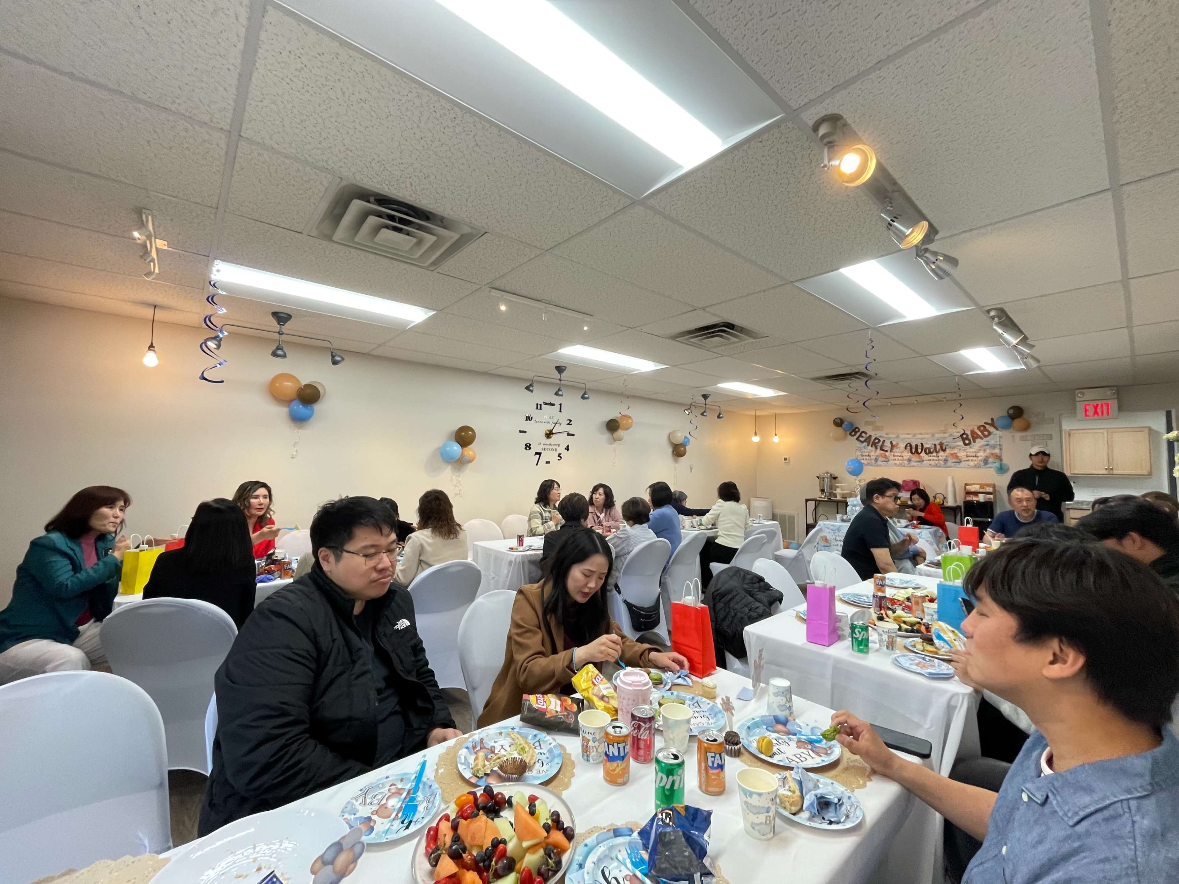 A group of people is sitting at tables covered with food and drinks in a decorated indoor space.
