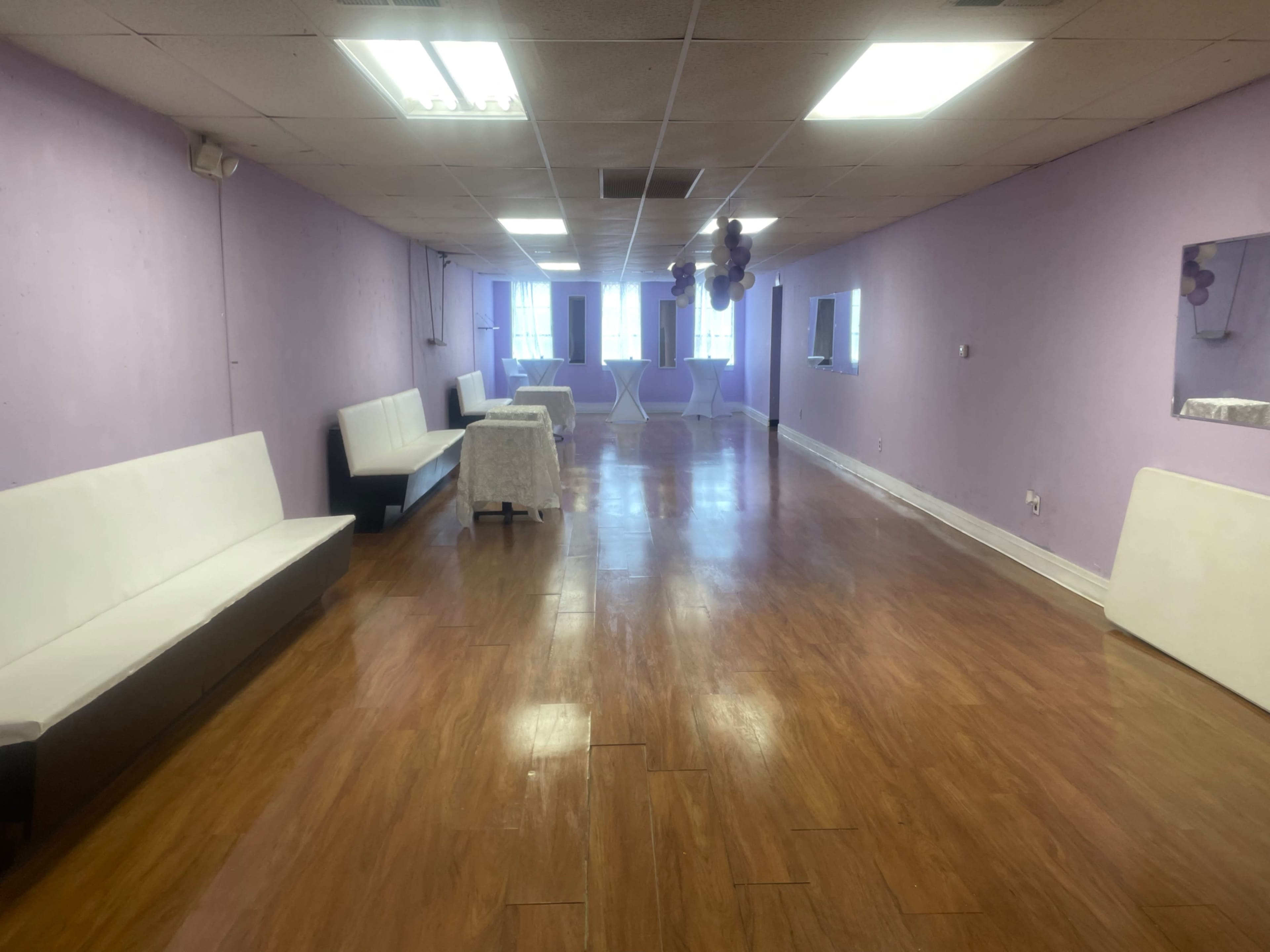 An empty event space with lavender walls, several white benches along the sides, and a polished wooden floor.