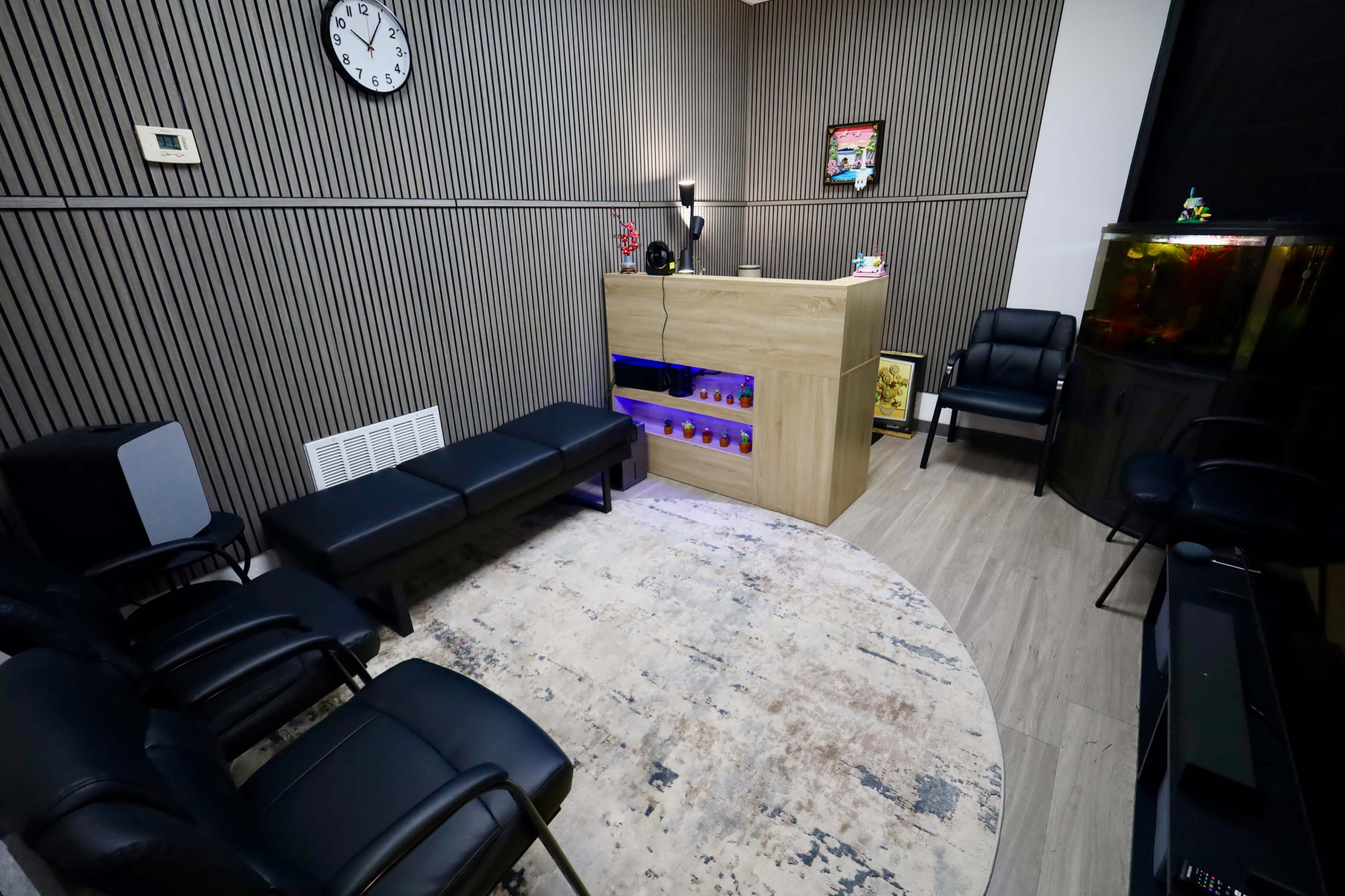 The image shows a modern waiting room with black chairs, a wooden reception desk with colorful displays, and a large aquarium in the corner.