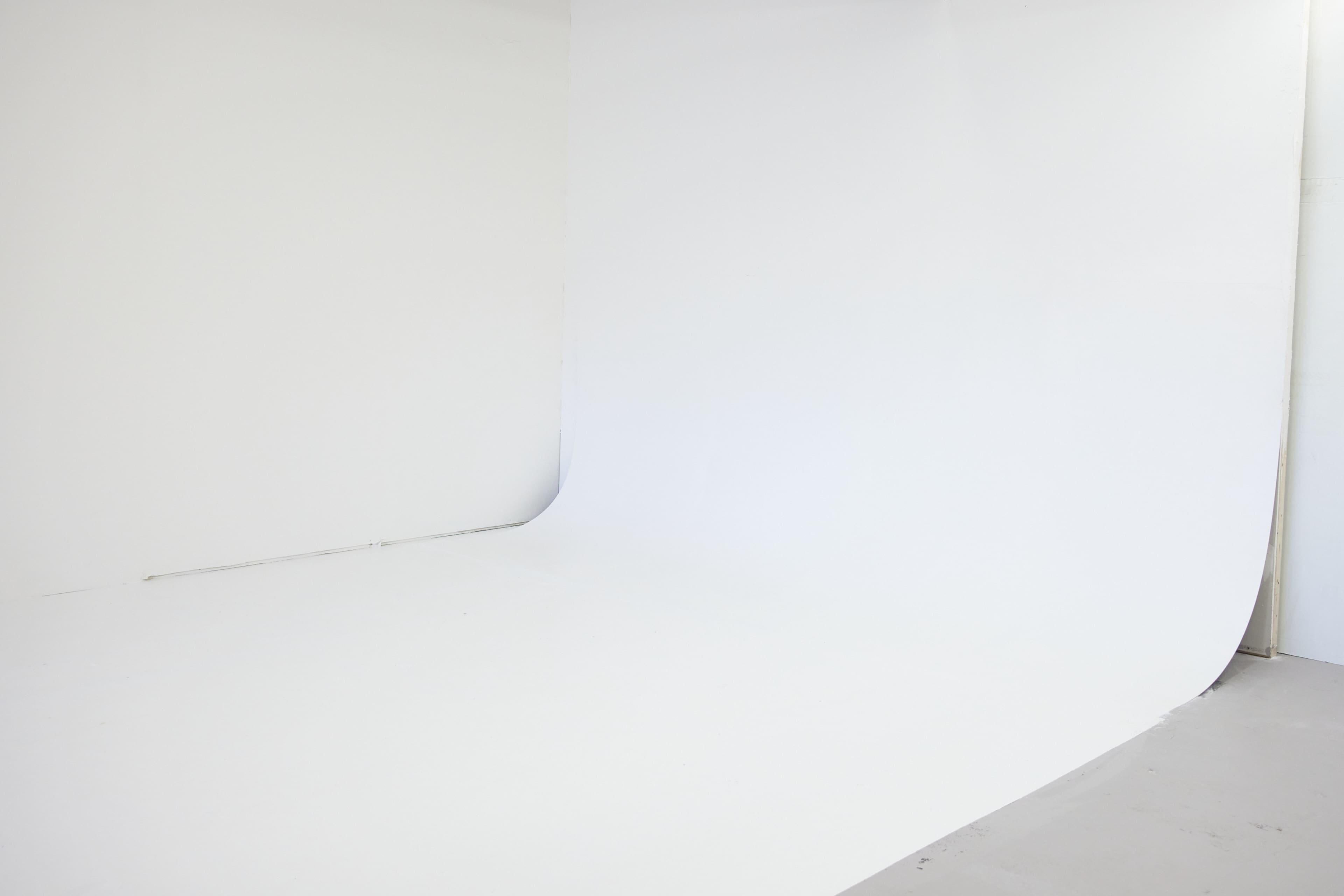 The image shows a minimalist white studio background with a seamless backdrop and a smooth floor.