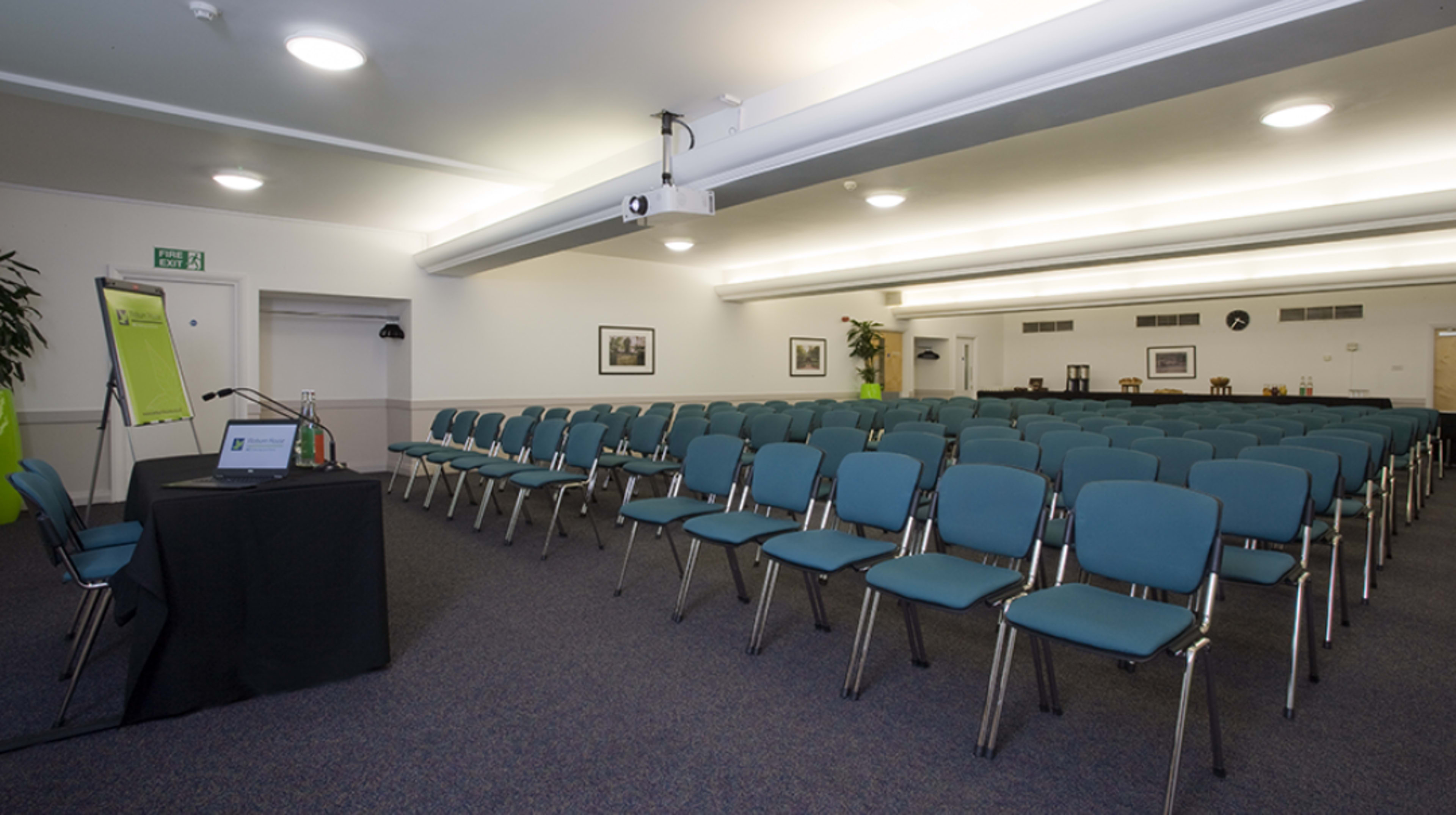 A conference room set up with rows of chairs facing a presentation area and a table with a laptop and water.