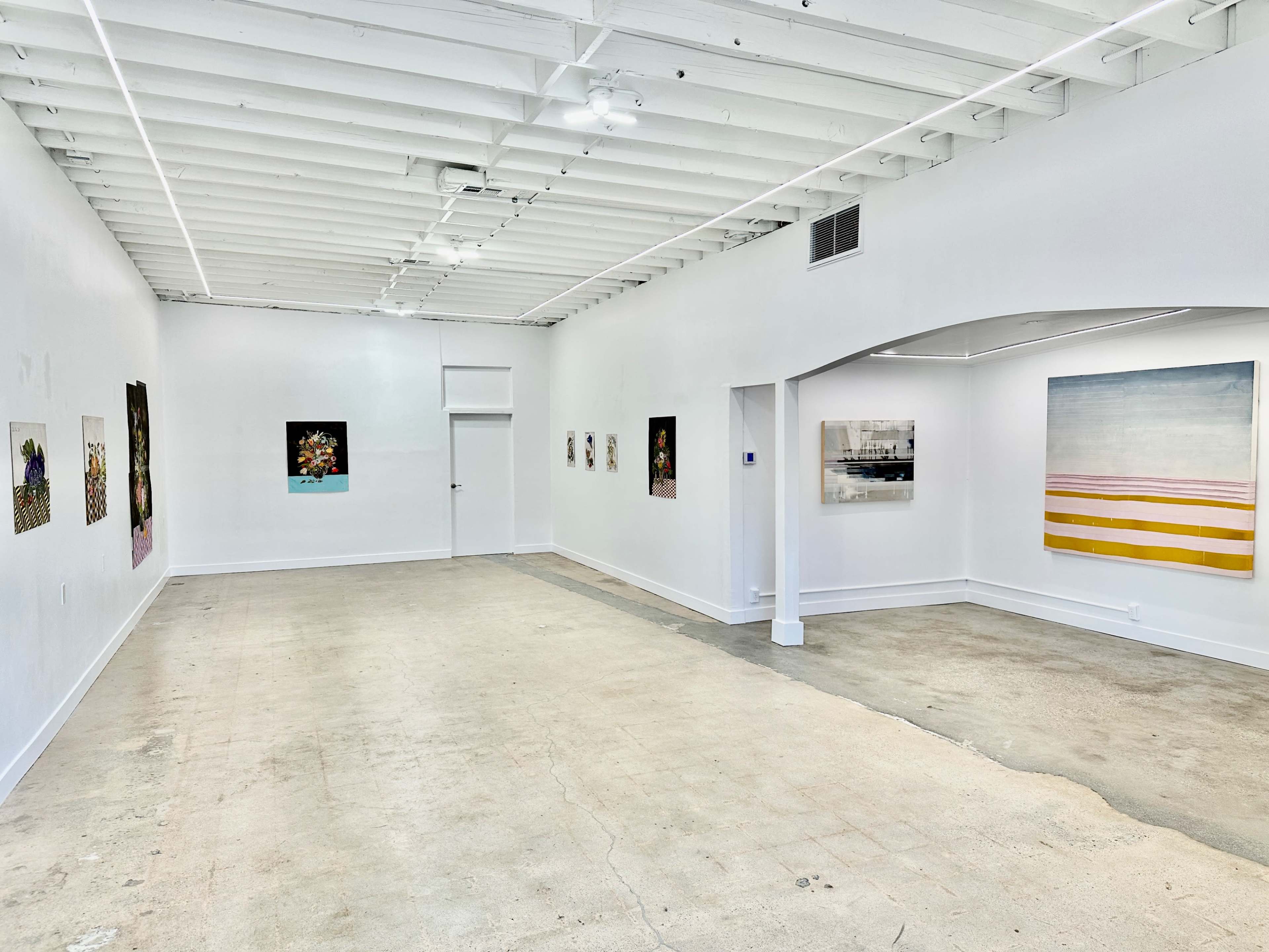 A spacious art gallery with white walls, showcasing various artworks hung on the walls and a concrete floor.