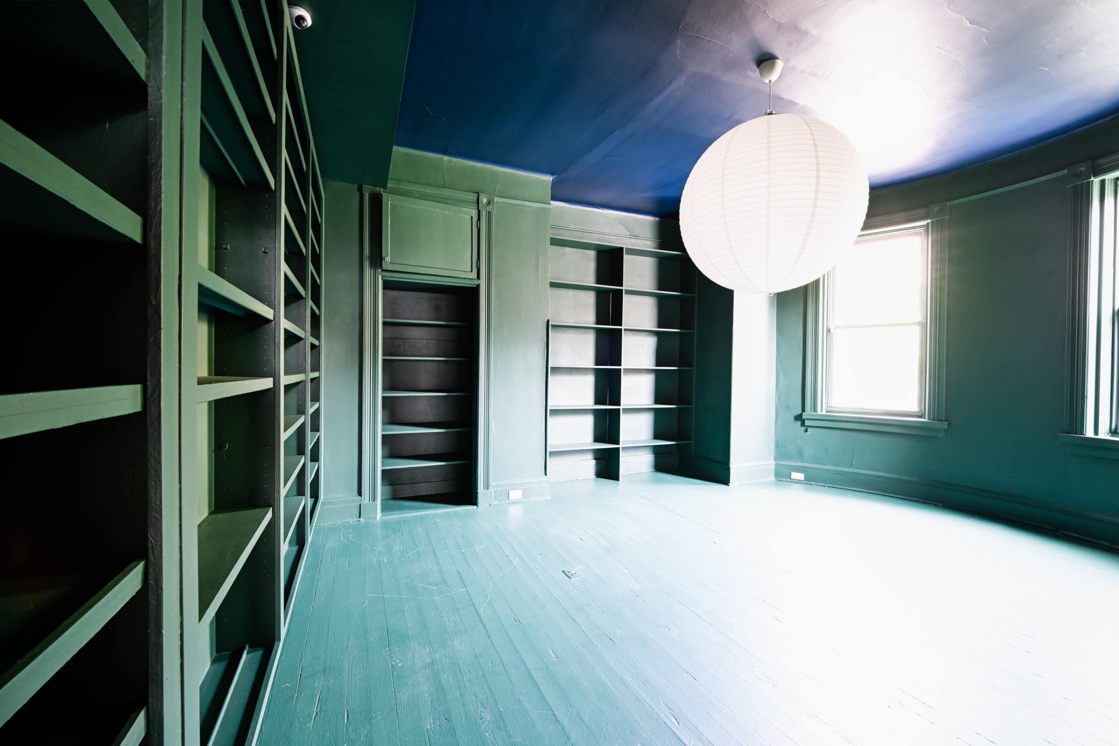 The image shows a spacious, empty room with green walls, built-in shelves, and a large paper lantern hanging from the ceiling.