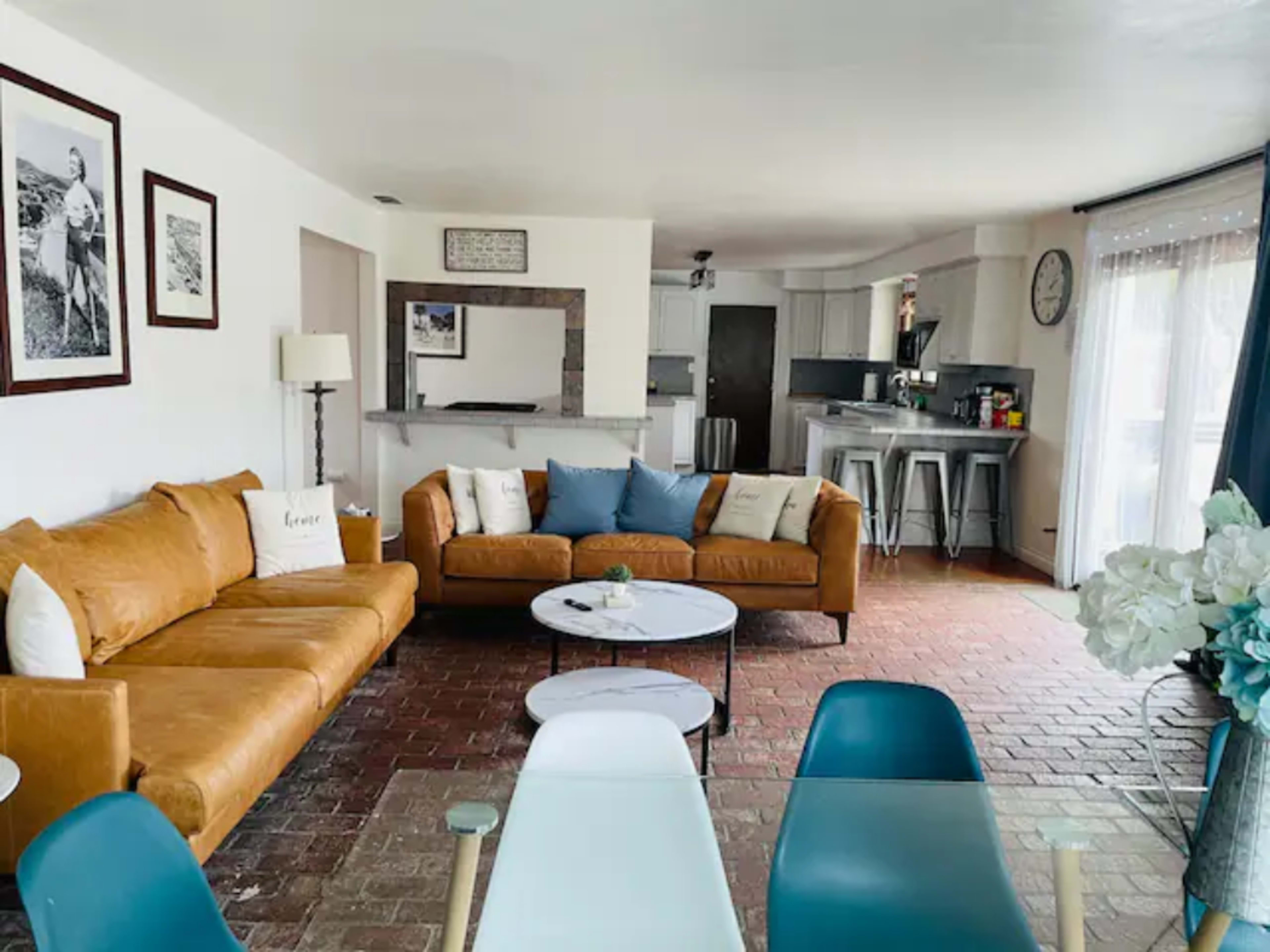 A living room with a brown sectional sofa, a round coffee table, and a dining area featuring modern chairs and a kitchen in the background.